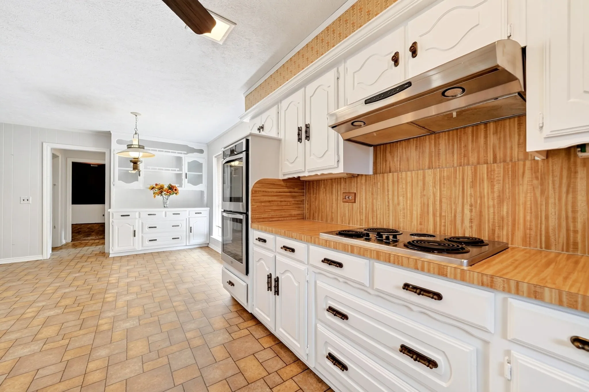 Chef's kitchen featuring white cabinetry with black hardware, wood-finish countertops, professional-grade gas cooktop, dual wall-mounted ovens, and a wood-finish backsplash