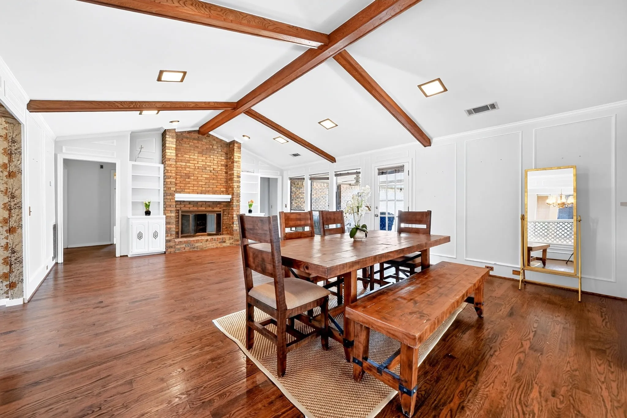 Varnished wood-finish flooring, vaulted ceilings with exposed wood beams, brick-clad fireplace with mantel, built-in shelving, and panel molding