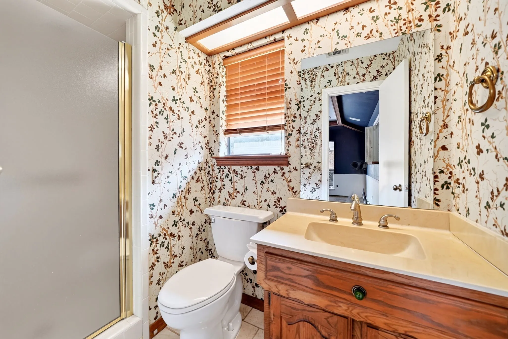 Bathroom featuring a wood-finish vanity with an integrated sink, polished brass-finish faucet, and a wall-mounted mirror