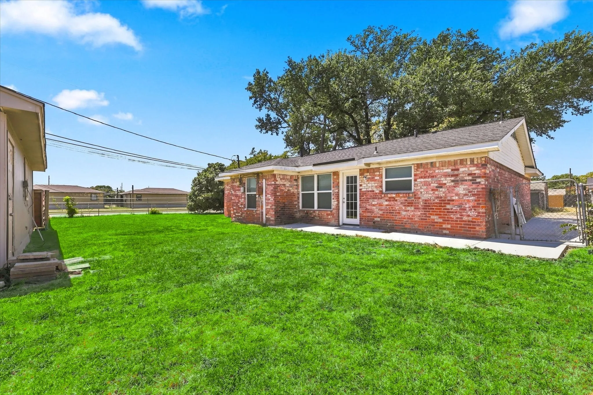 Expansive green lawn with a red brick exterior, multiple windows, and a white back door leading to a concrete patio
