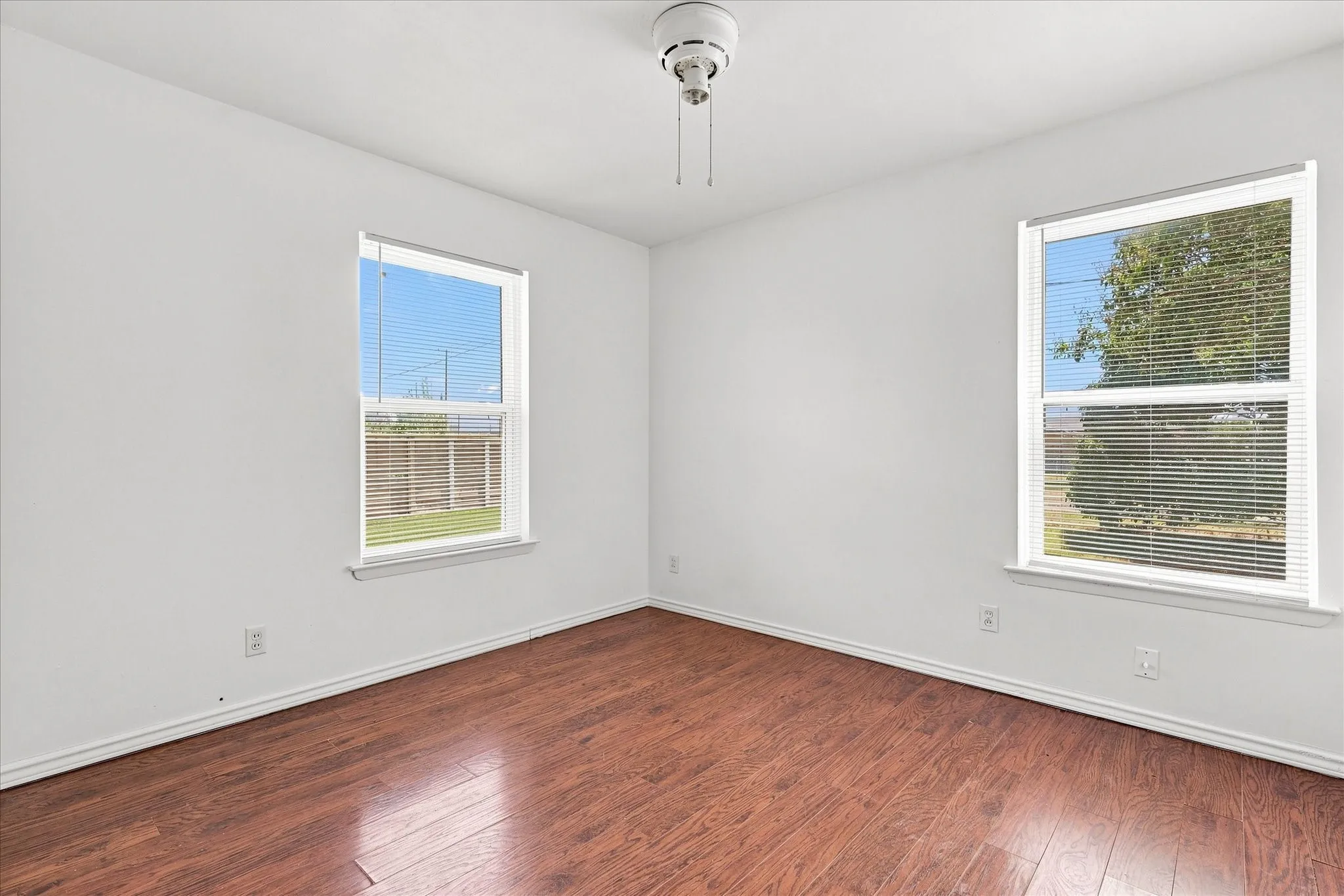 Wood-finish flooring, white walls, two windows with blinds, and a ceiling fan