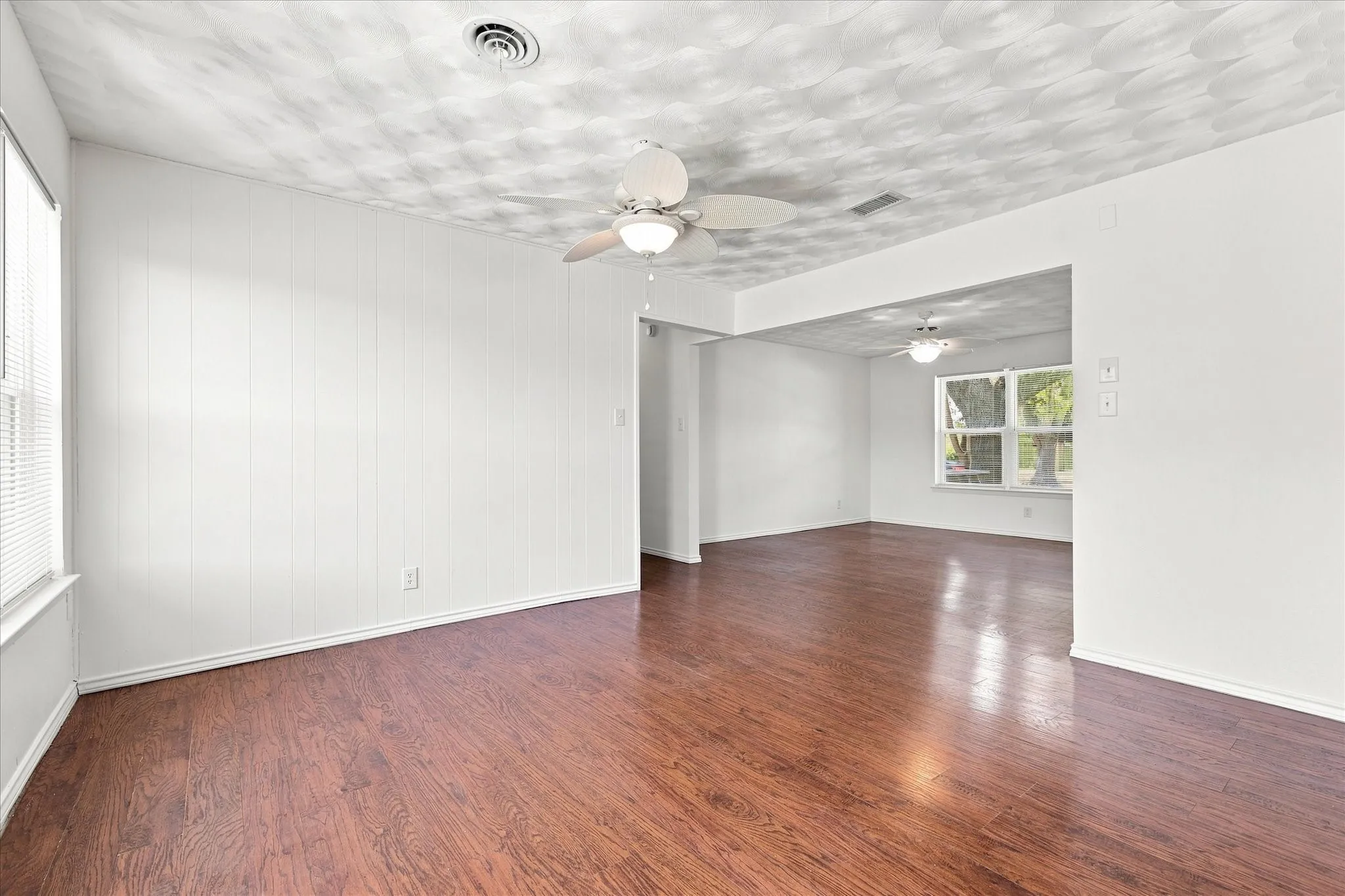 Wood-finish flooring, white paneling, ceiling fan with integrated lighting, and multiple windows