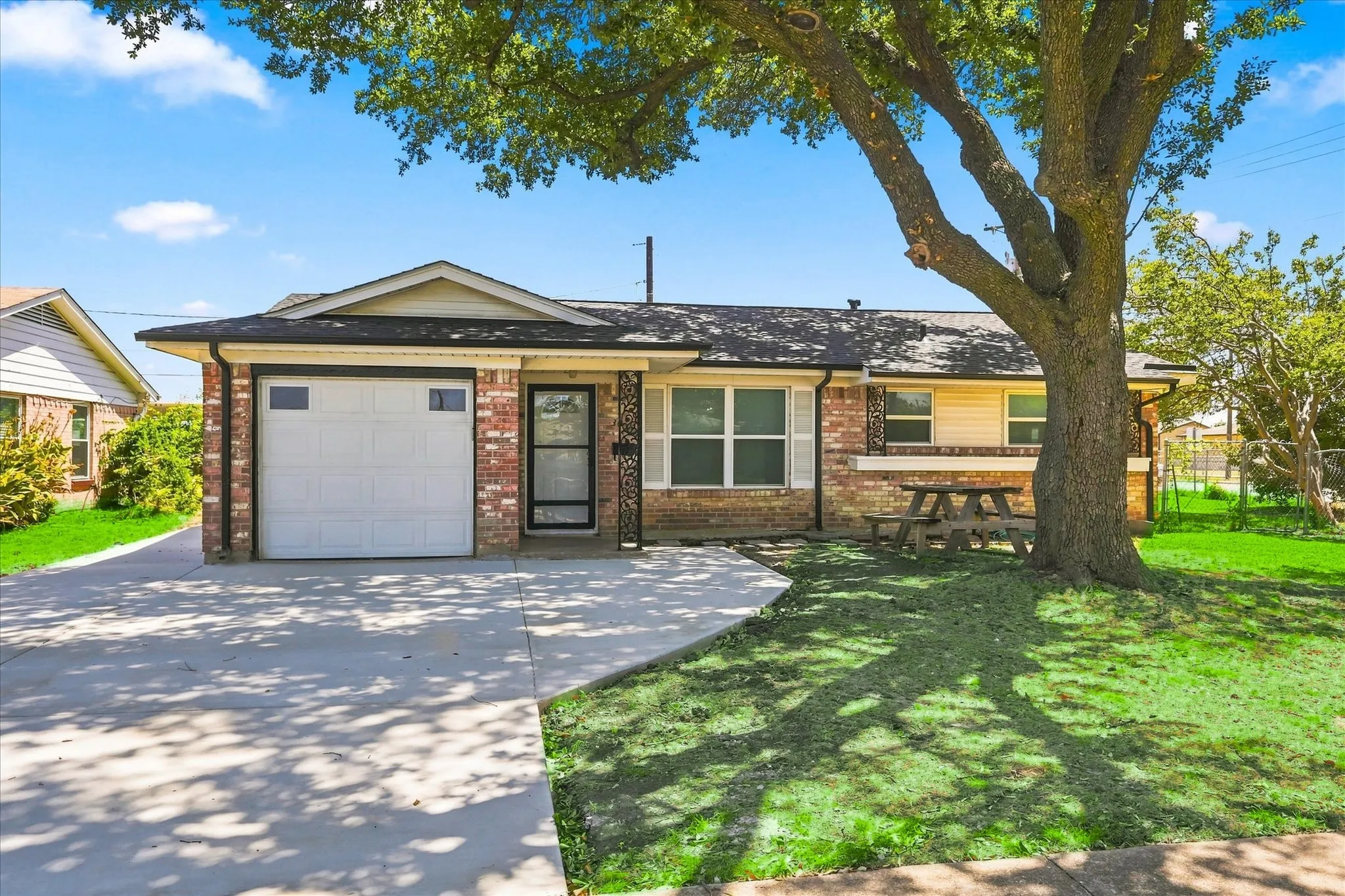 Brick and siding exterior with an attached garage, paved driveway, and mature front yard tree