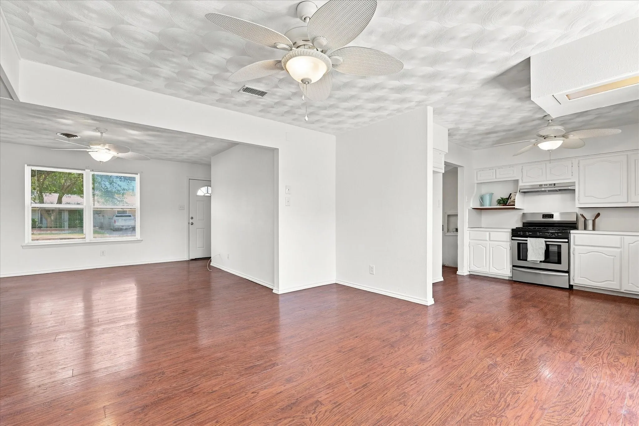 Wood-finish flooring throughout, white cabinetry, stainless steel range, and multiple ceiling fans