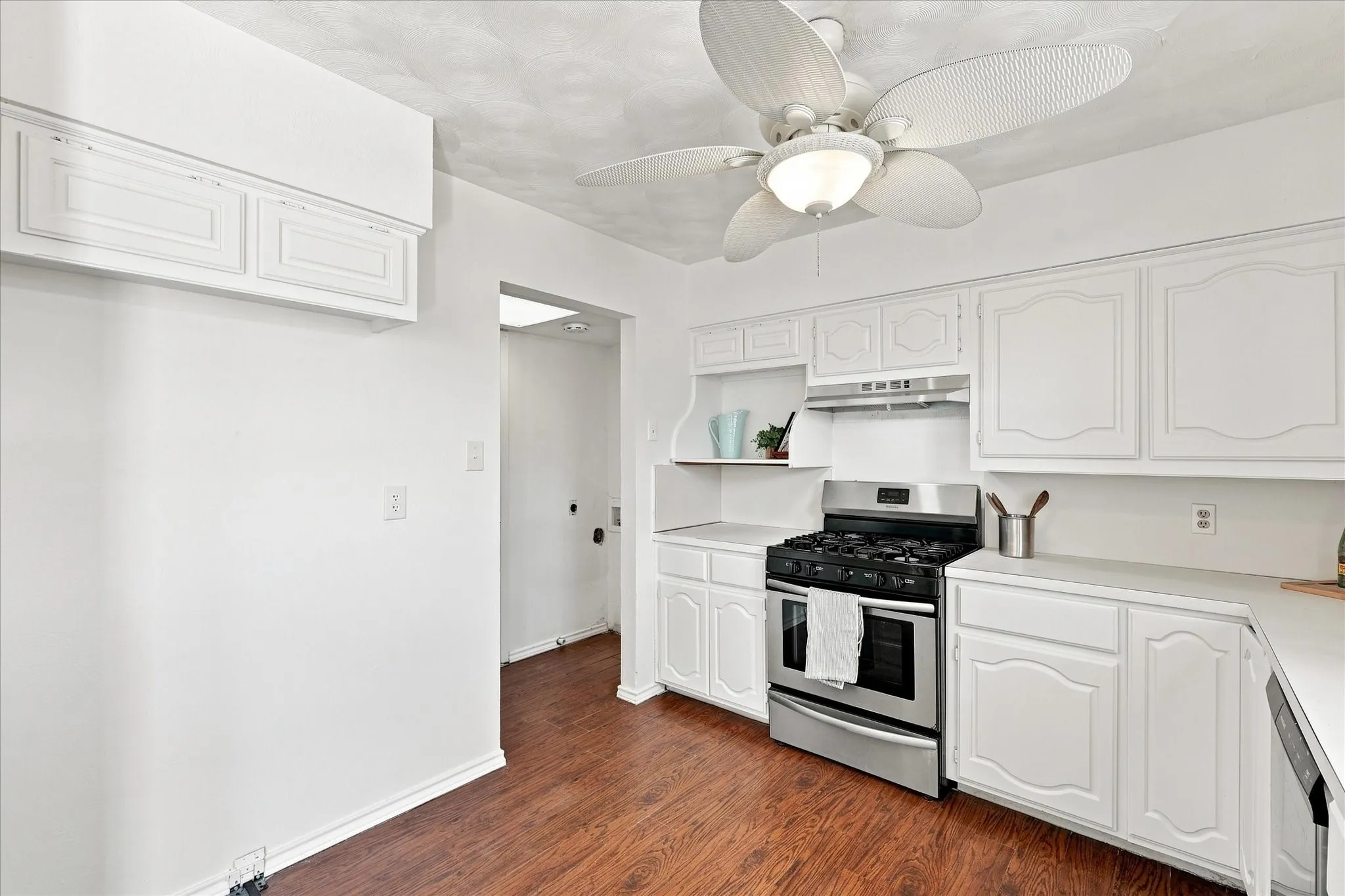 Kitchen featuring wood-finish flooring, white cabinetry, a stainless steel range, and a ceiling fan with integrated lighting