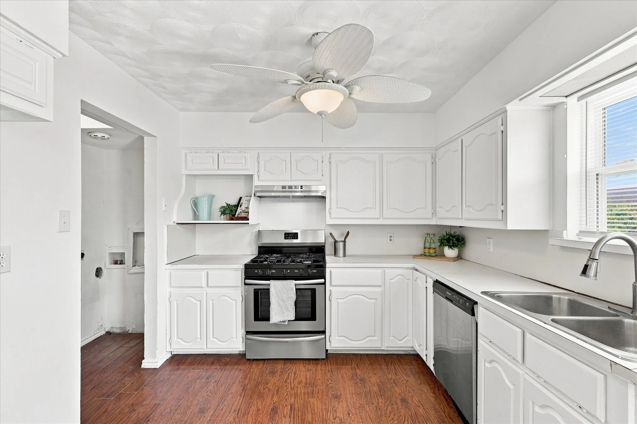 Kitchen featuring wood-finish flooring, white cabinetry, stainless steel appliances, and a double basin sink