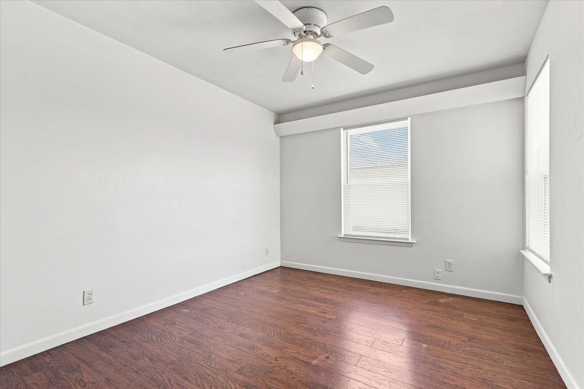 Wood-finish flooring, ceiling fan, and two windows with blinds