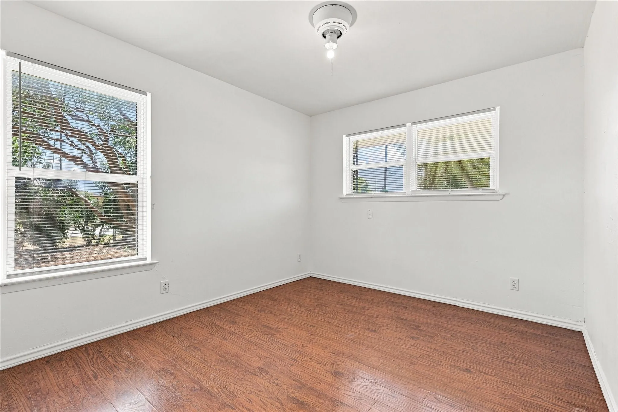 Wood-finish flooring with white baseboards, multiple windows, and a ceiling-mounted light fixture