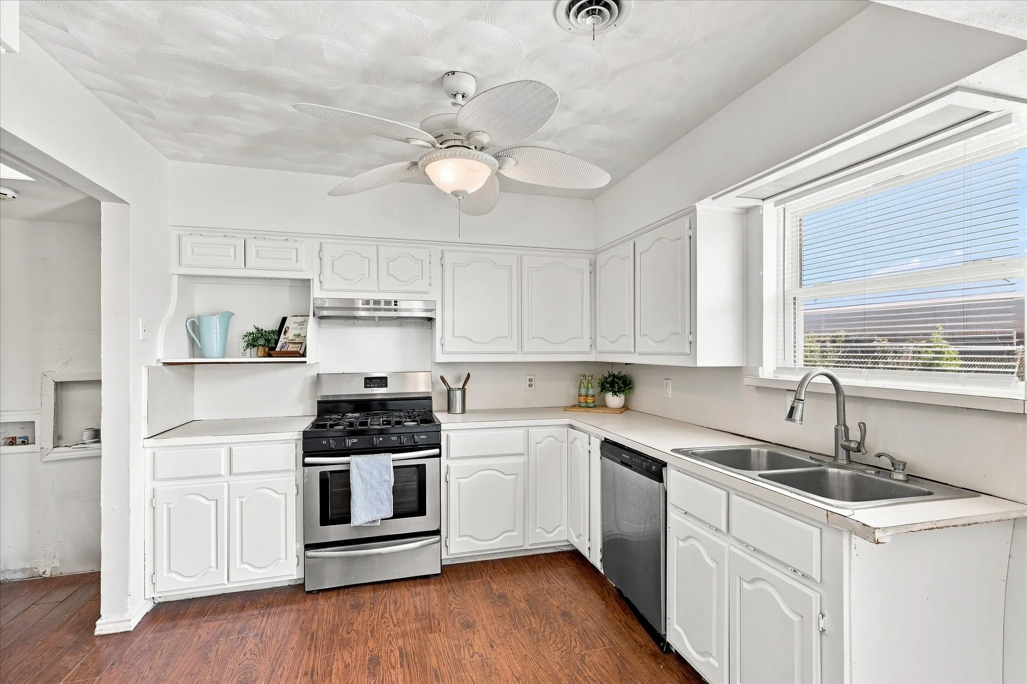 Kitchen featuring white cabinetry, stainless steel range, stainless steel dishwasher, double basin sink, and wood-finish flooring