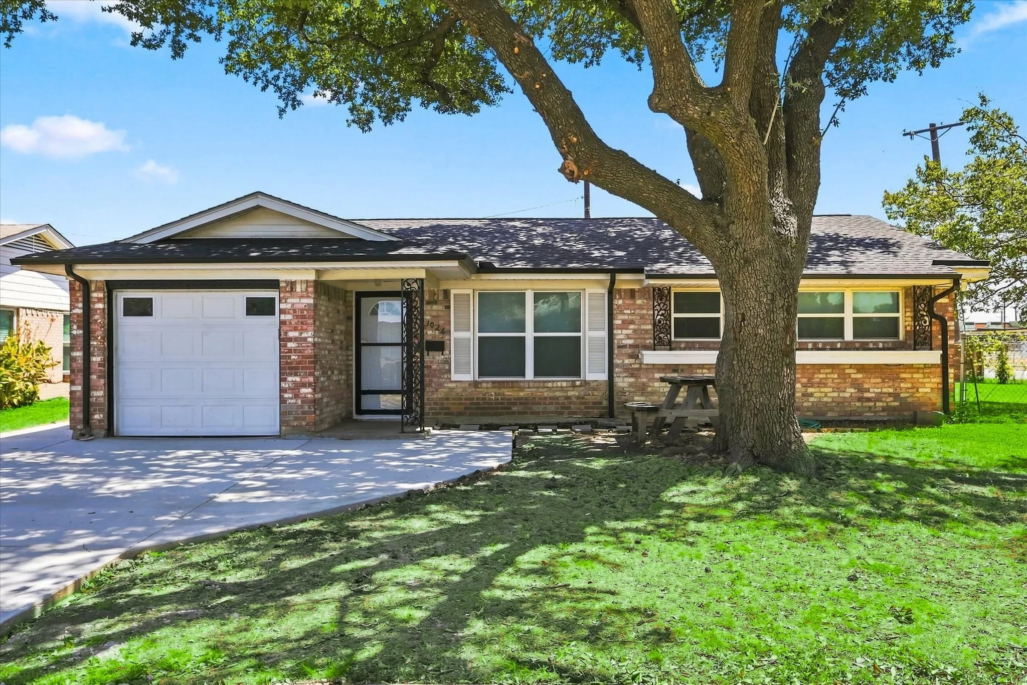 Brick exterior with a white garage door, concrete driveway, and a mature tree providing shade