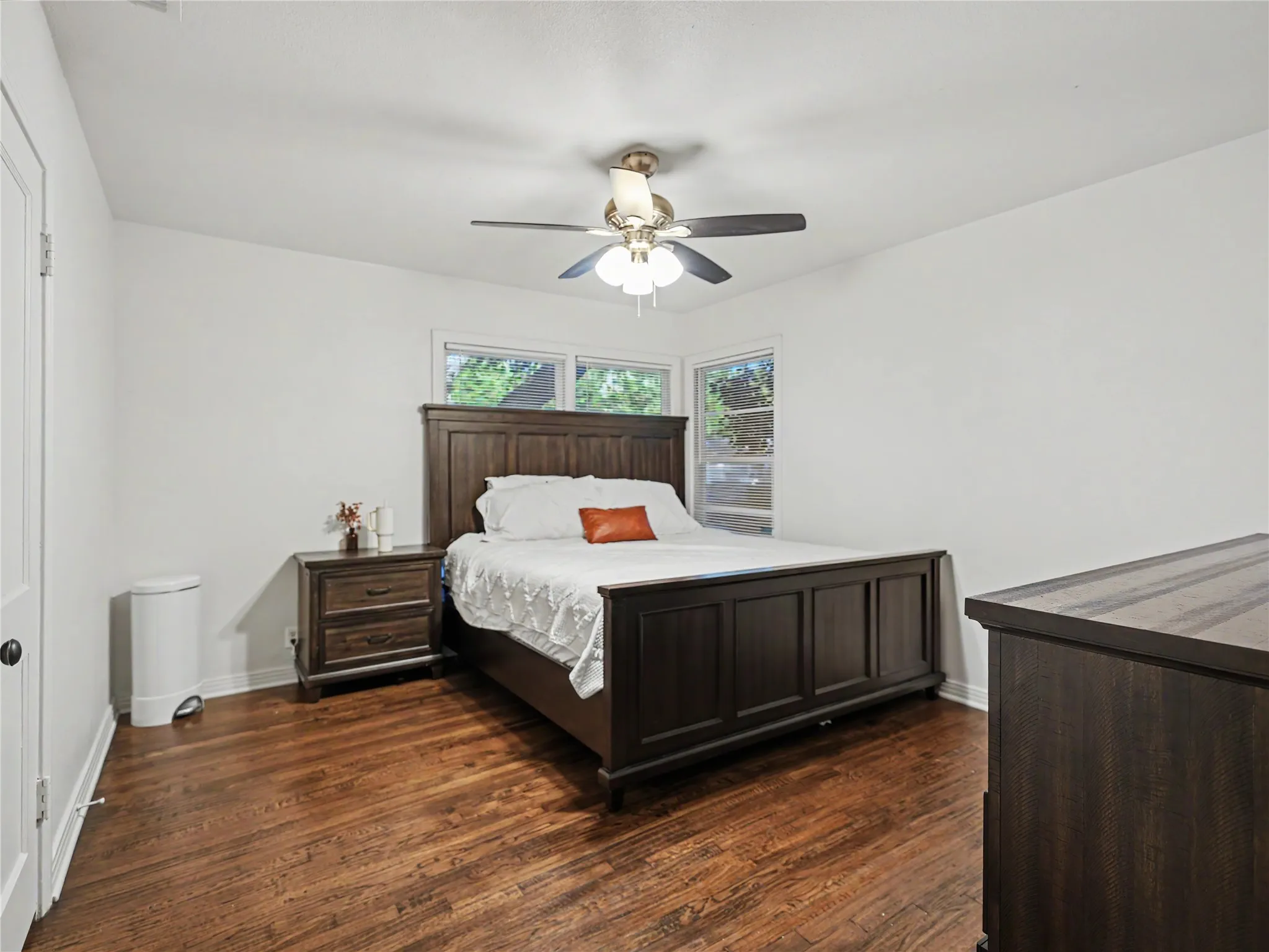 Hardwood flooring, corner windows, white walls, and a ceiling fan with light fixture