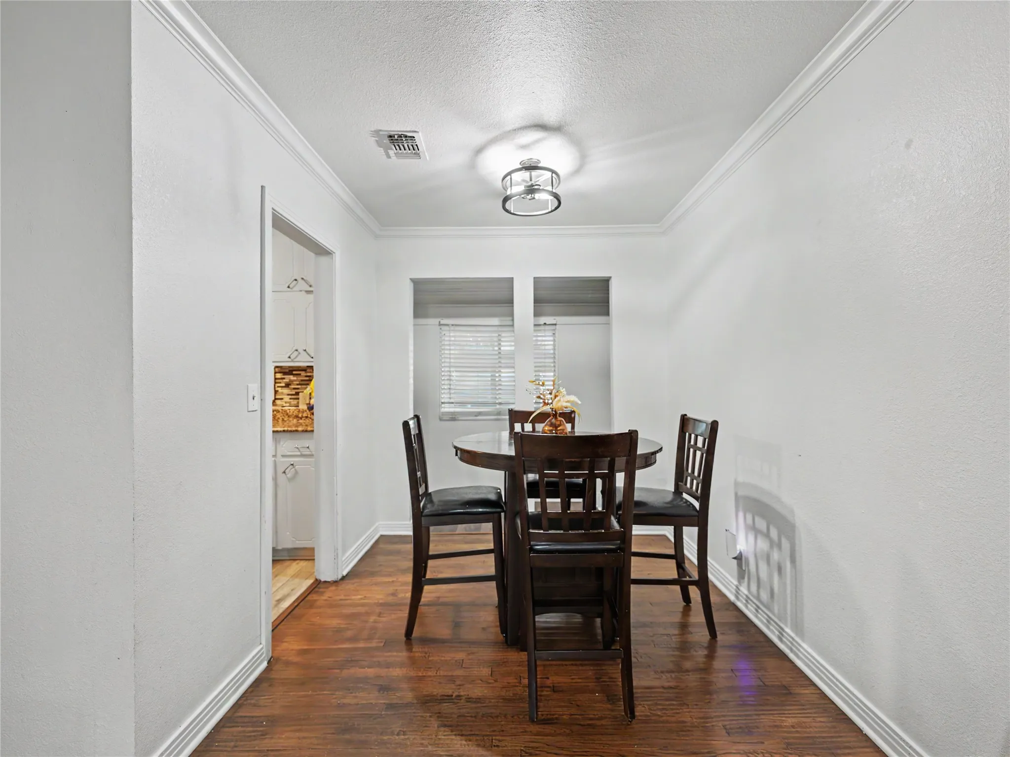 Wood-finish flooring with white baseboards, crown molding, and a modern ceiling light fixture