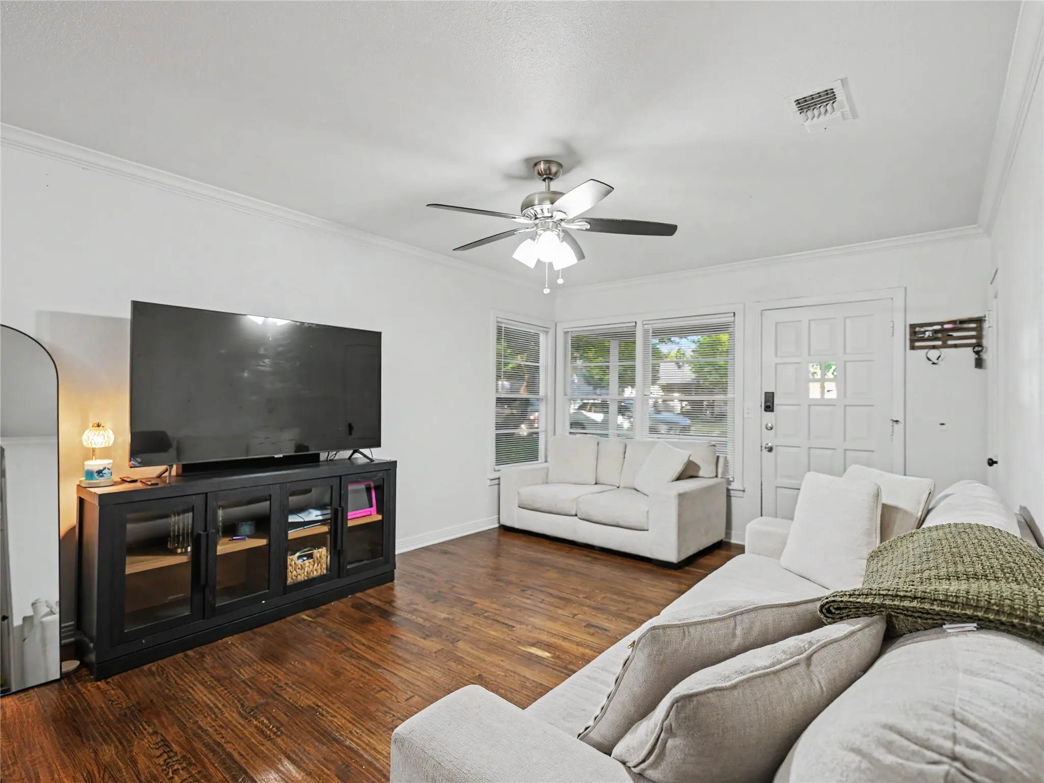 Hardwood flooring, crown molding, white paneled entrance door, multiple windows, and a ceiling fan with integrated lighting