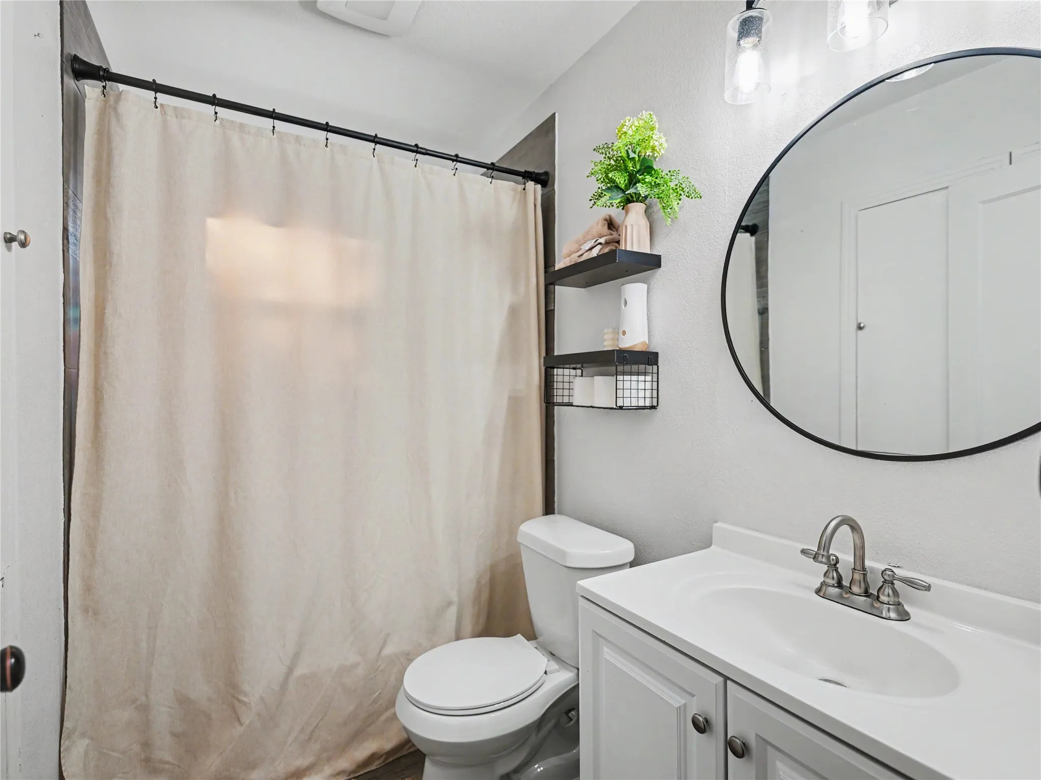 White vanity with cabinet storage, round mirror, and wall-mounted light fixture