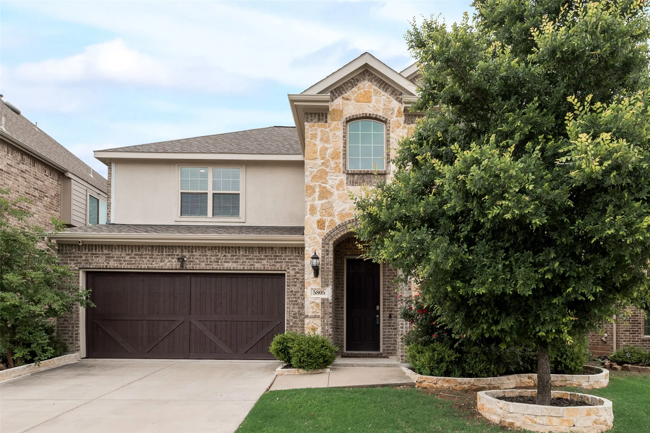 Traditional-style house featuring a shingled roof, brick siding, a garage, stucco siding, and concrete driveway