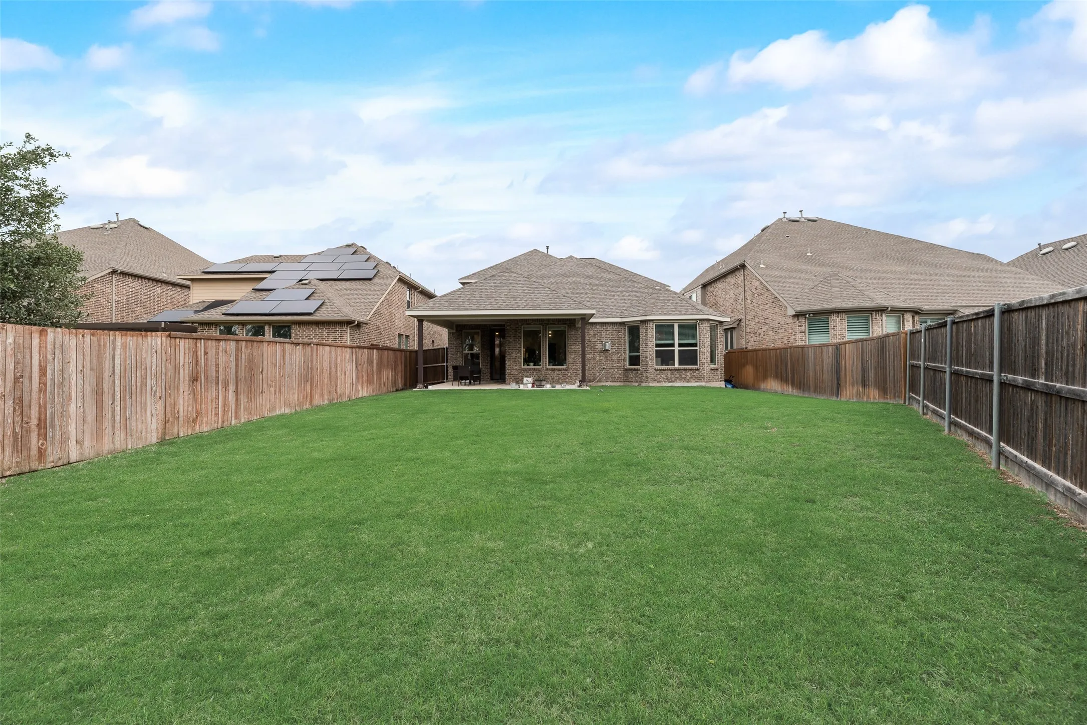 Rear view of property with a patio, a fenced backyard, roof with shingles, brick siding, and a lawn