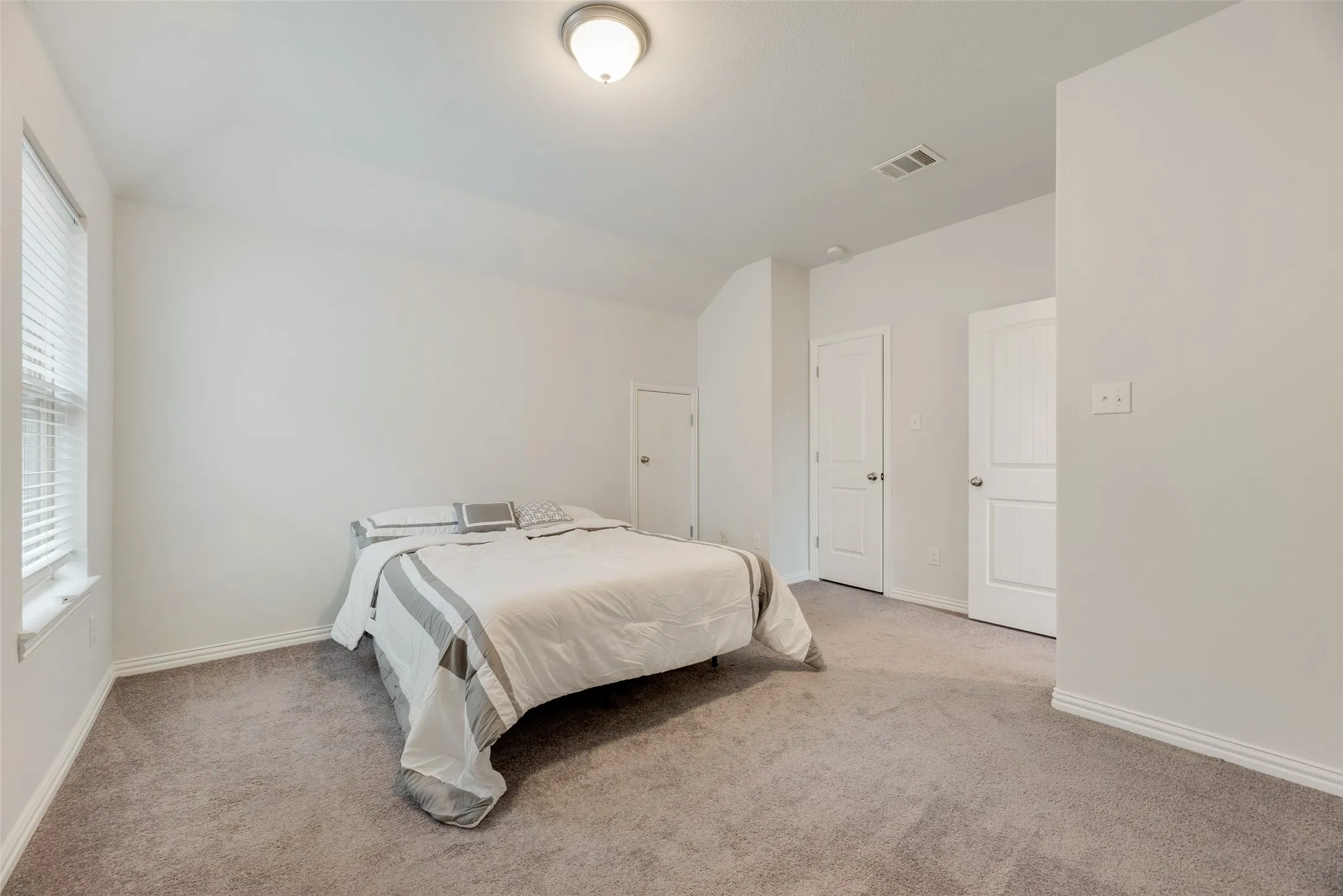 Carpeted bedroom with visible vents, baseboards, and vaulted ceiling