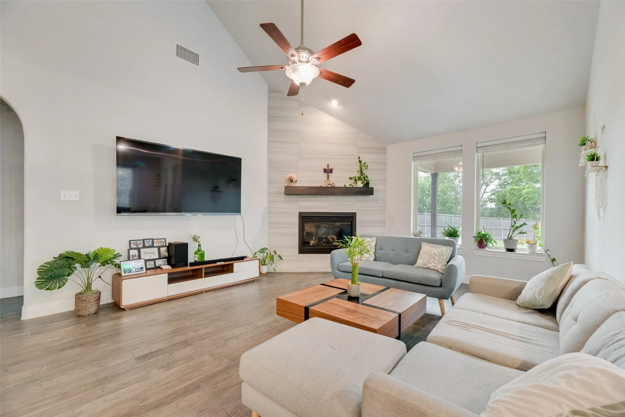 Living room featuring ceiling fan, arched walkways, high vaulted ceiling, wood finished floors, and visible vents