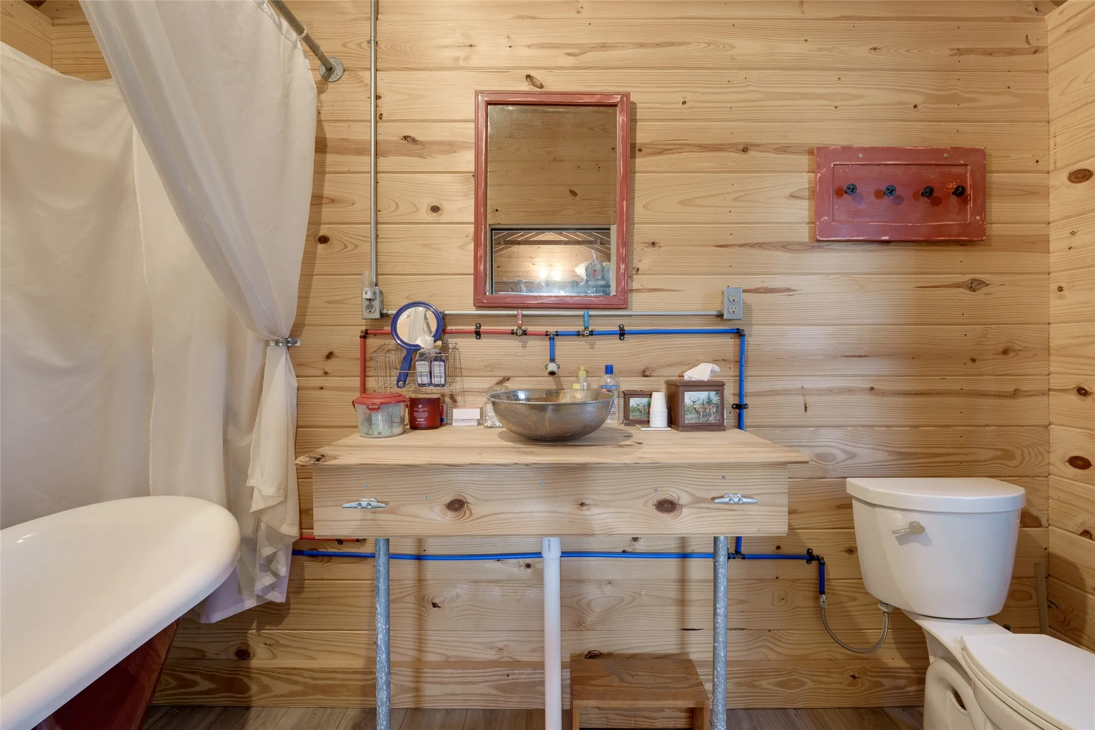 Wood plank wall finishes, wood-finish flooring, freestanding bathtub, wood vanity with basin sink, and a wall-mounted mirror