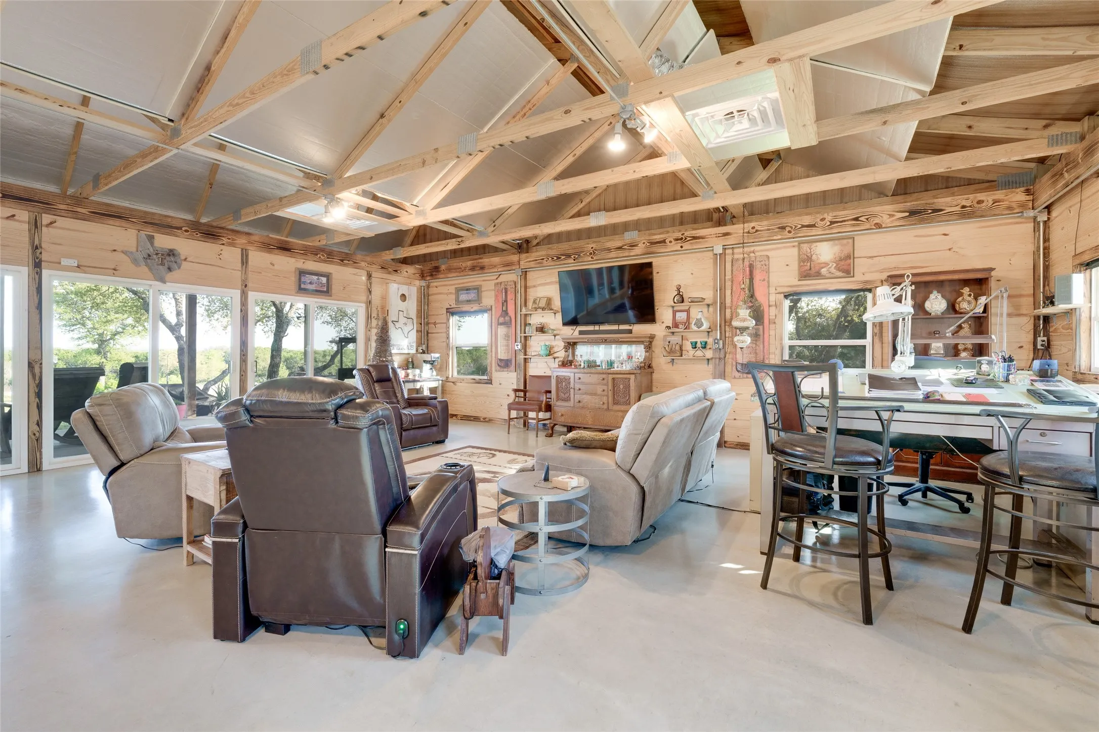 Vaulted wood-beam ceilings, exposed wood walls, concrete flooring, large glass sliding doors, and built-in shelving