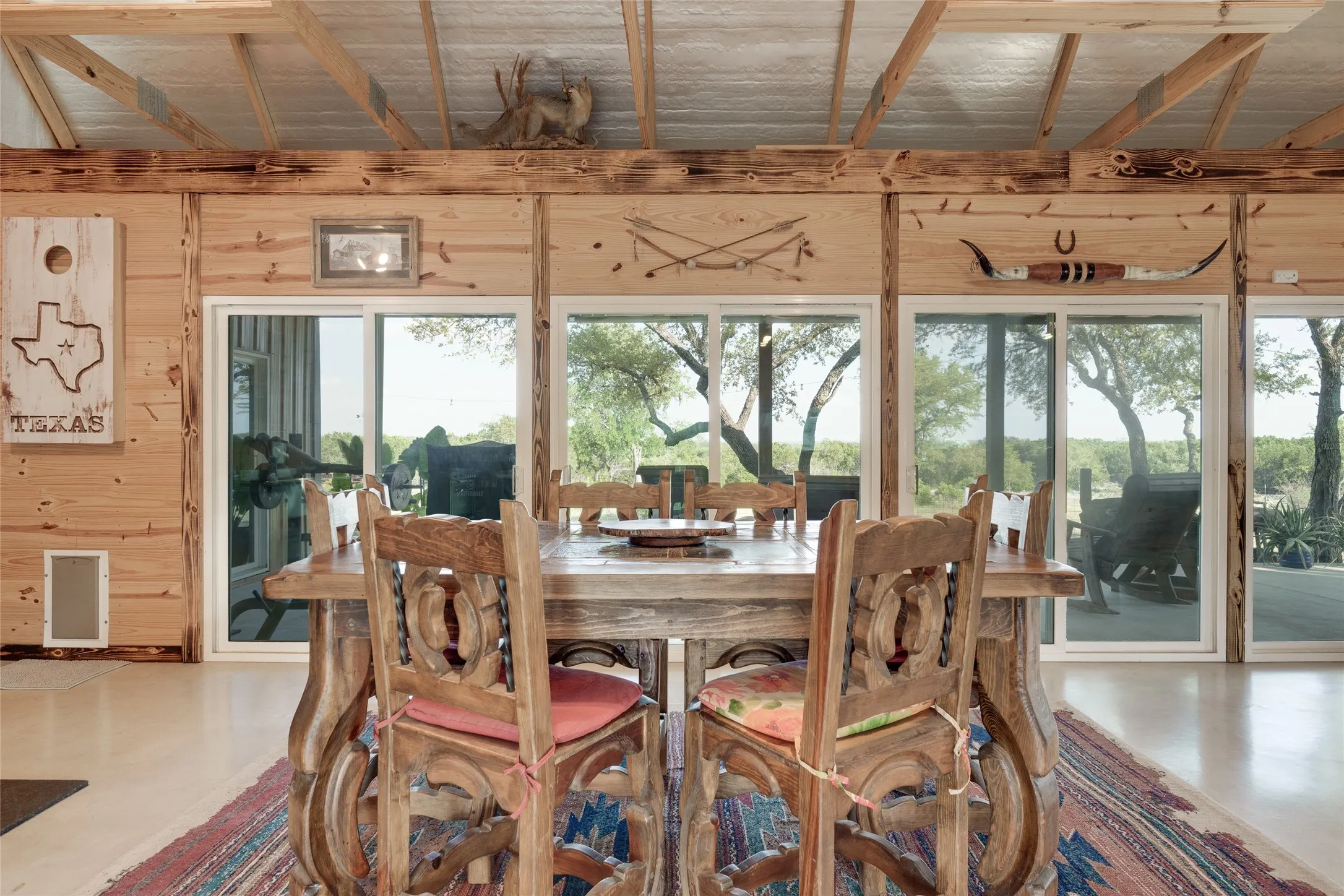 Wood-paneled interior walls, exposed wood beam ceiling, multiple sliding glass doors, concrete flooring