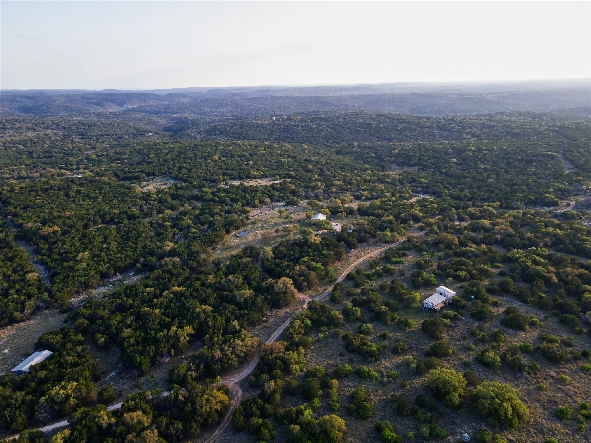 Expansive acreage featuring multiple structures, mature trees, and a distant tree-lined horizon