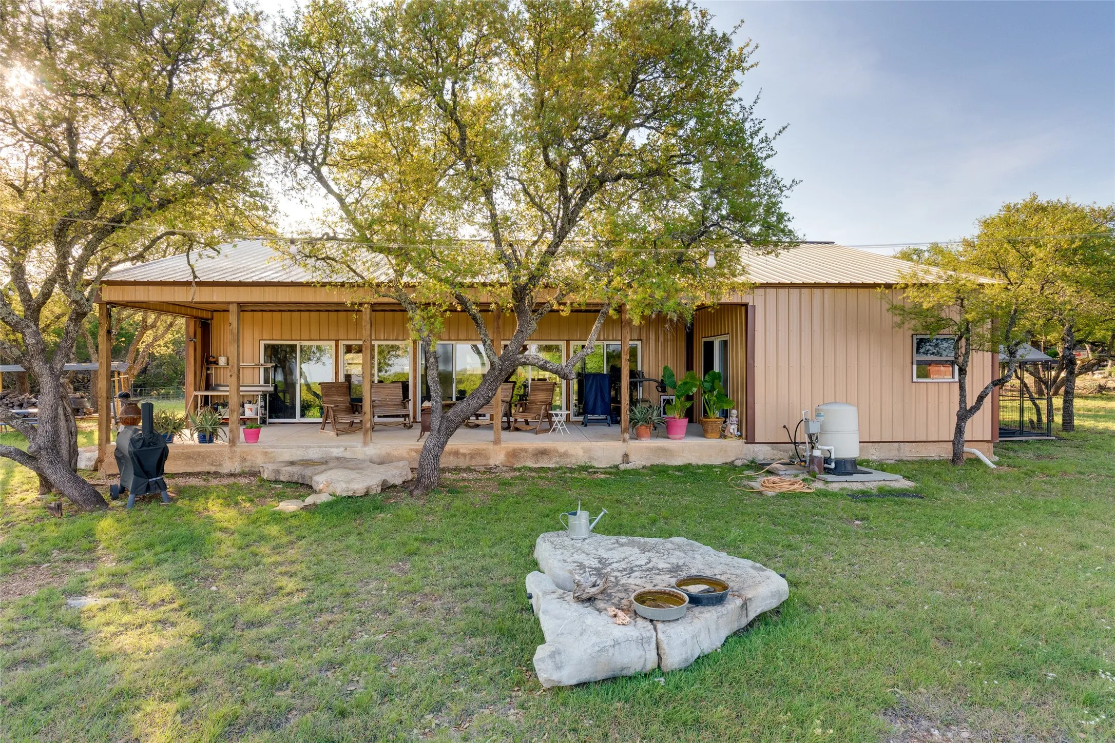 Extended covered patio, metal roof, sliding glass doors, side entry, and a spacious grassy yard
