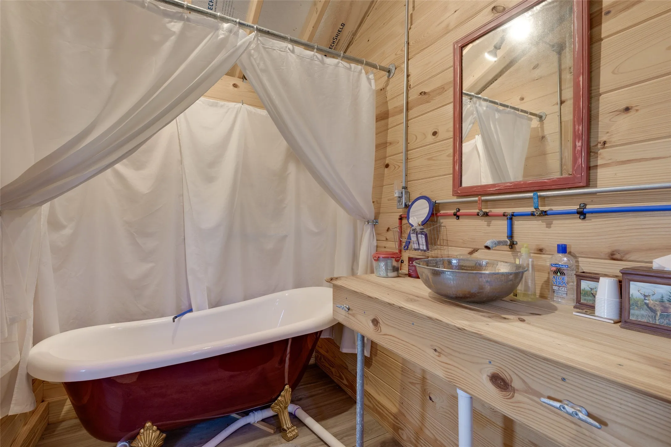 Clawfoot bathtub with red exterior finish, vessel sink, wood-finish countertop, and wall-mounted mirror