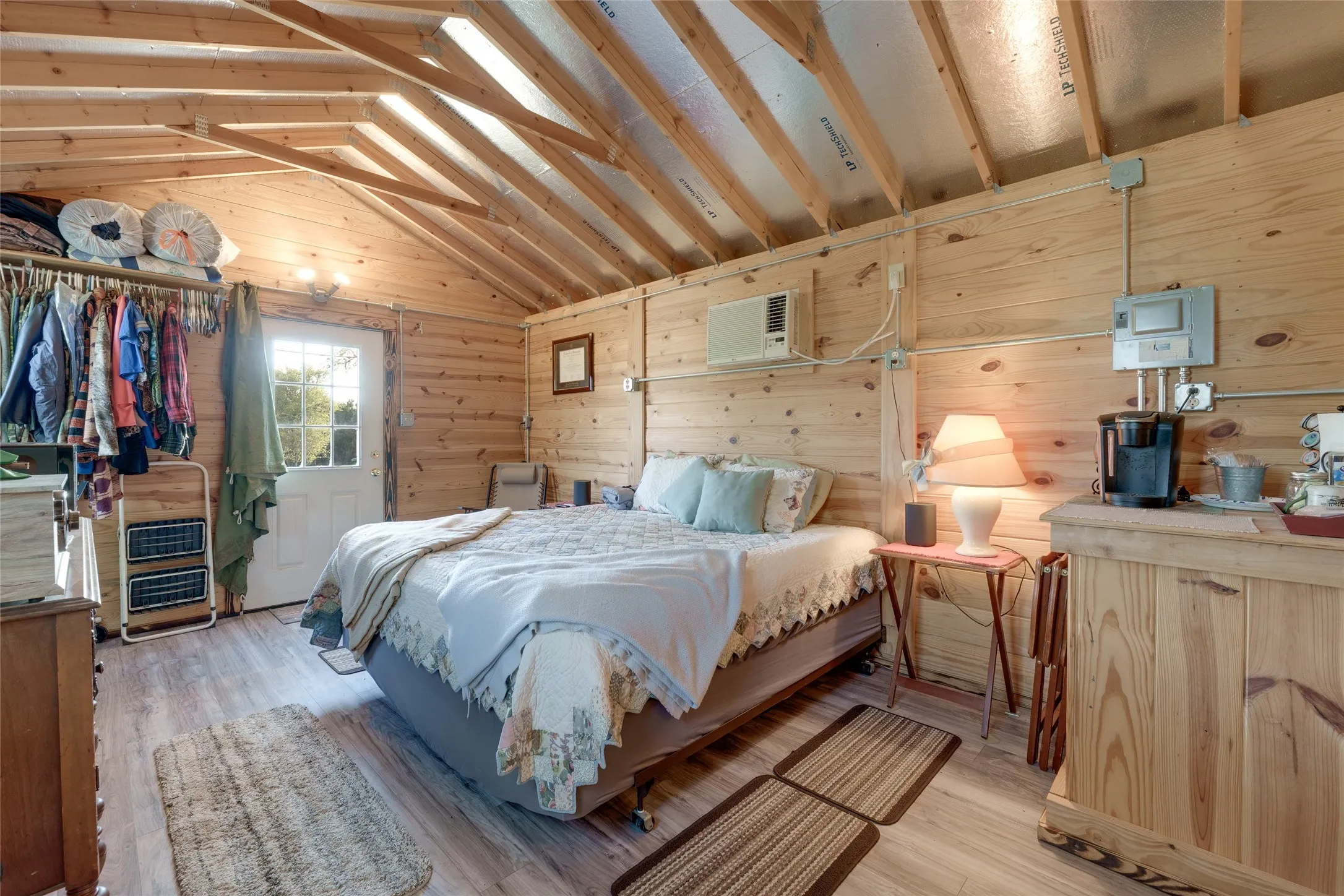 Wood-paneled interior walls, exposed ceiling rafters, wood-finish flooring, and a white paneled door with glass inserts