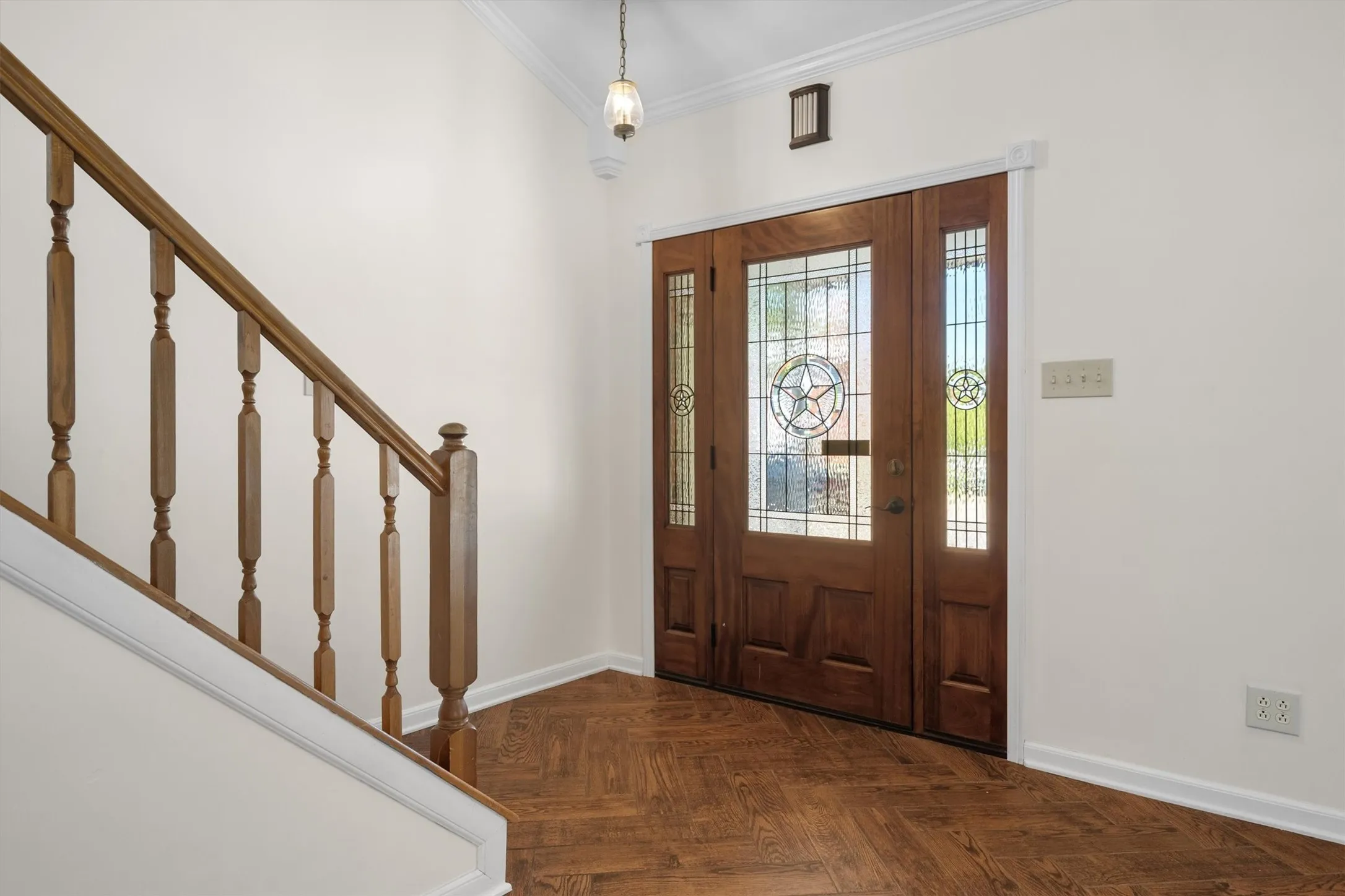 Elegant foyer entry featuring a rich wood staircase railing and herringbone-pattern flooring