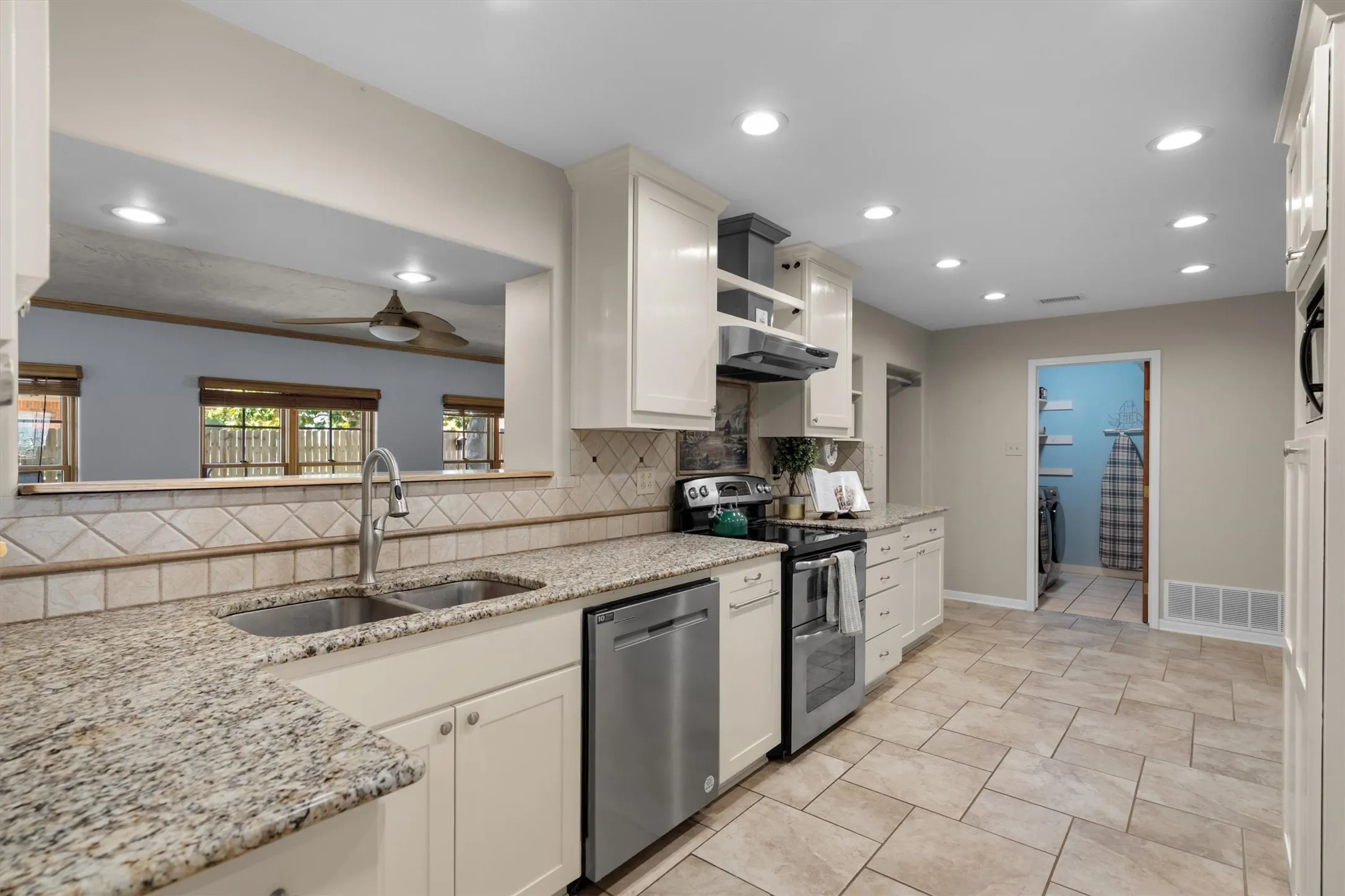 Galley-style kitchen view with granite counters, stainless sink, and hallway access