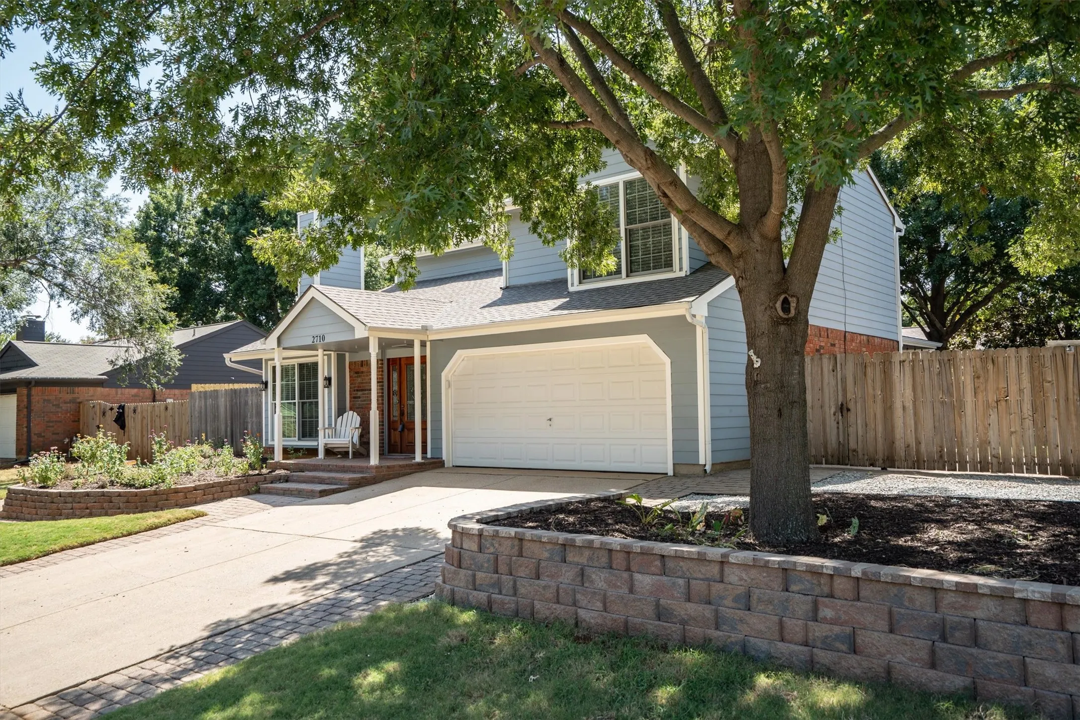 Inviting front elevation framed by mature shade trees and a stone-accented flower bed