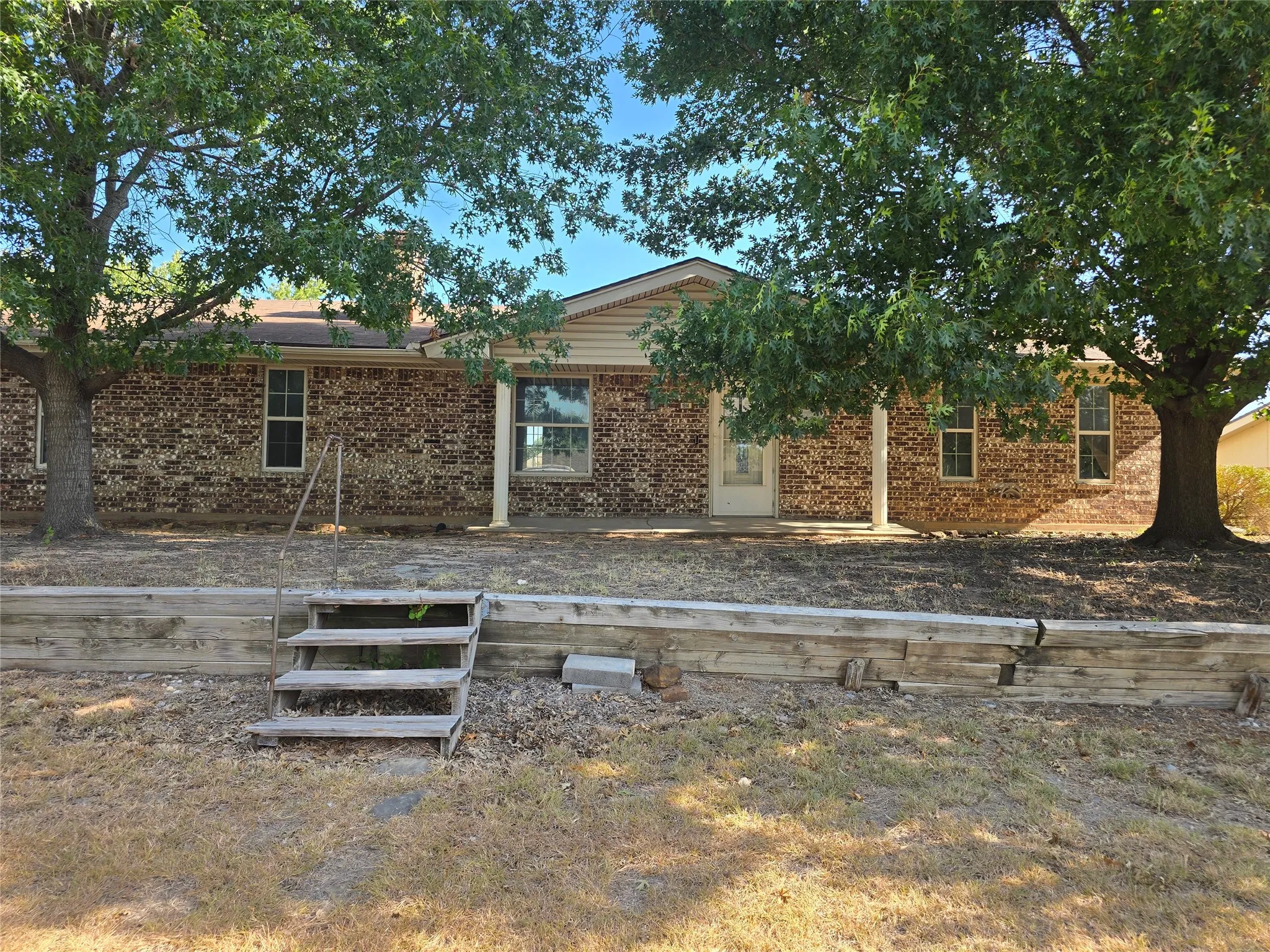 Brick exterior, covered entry, white paneled front door, white window trim, wood retaining wall