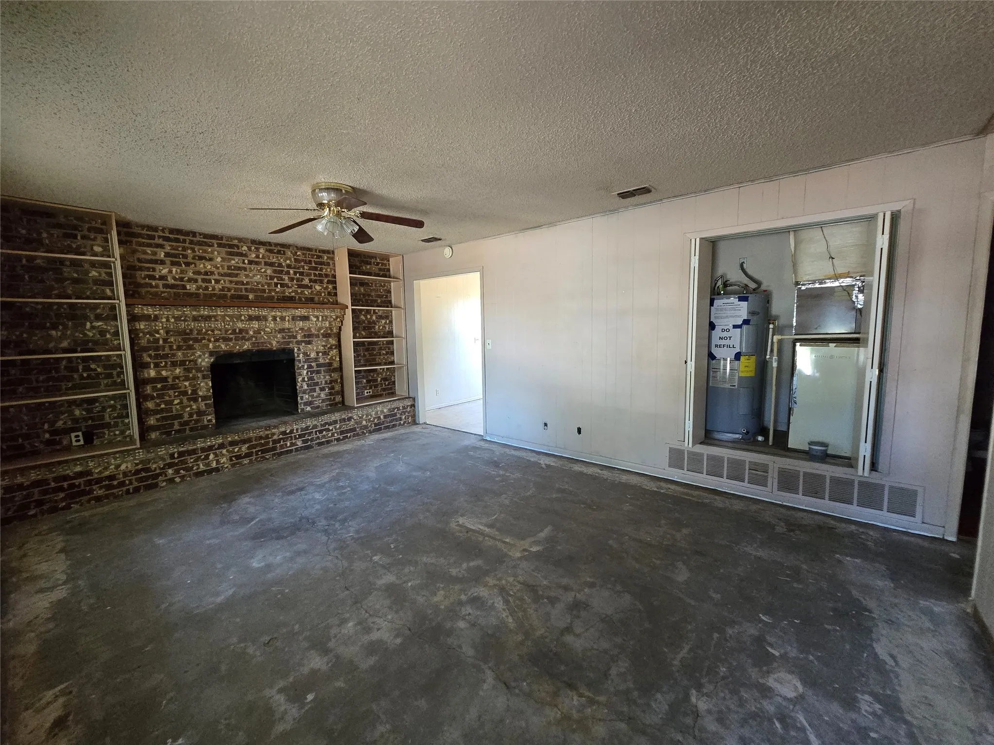 Brick fireplace with built-in shelving, paneled walls, and a ceiling fan