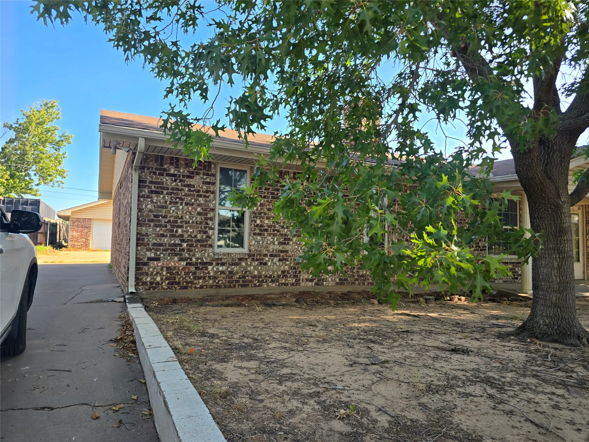 Brick exterior with white window trim, concrete driveway, and mature tree
