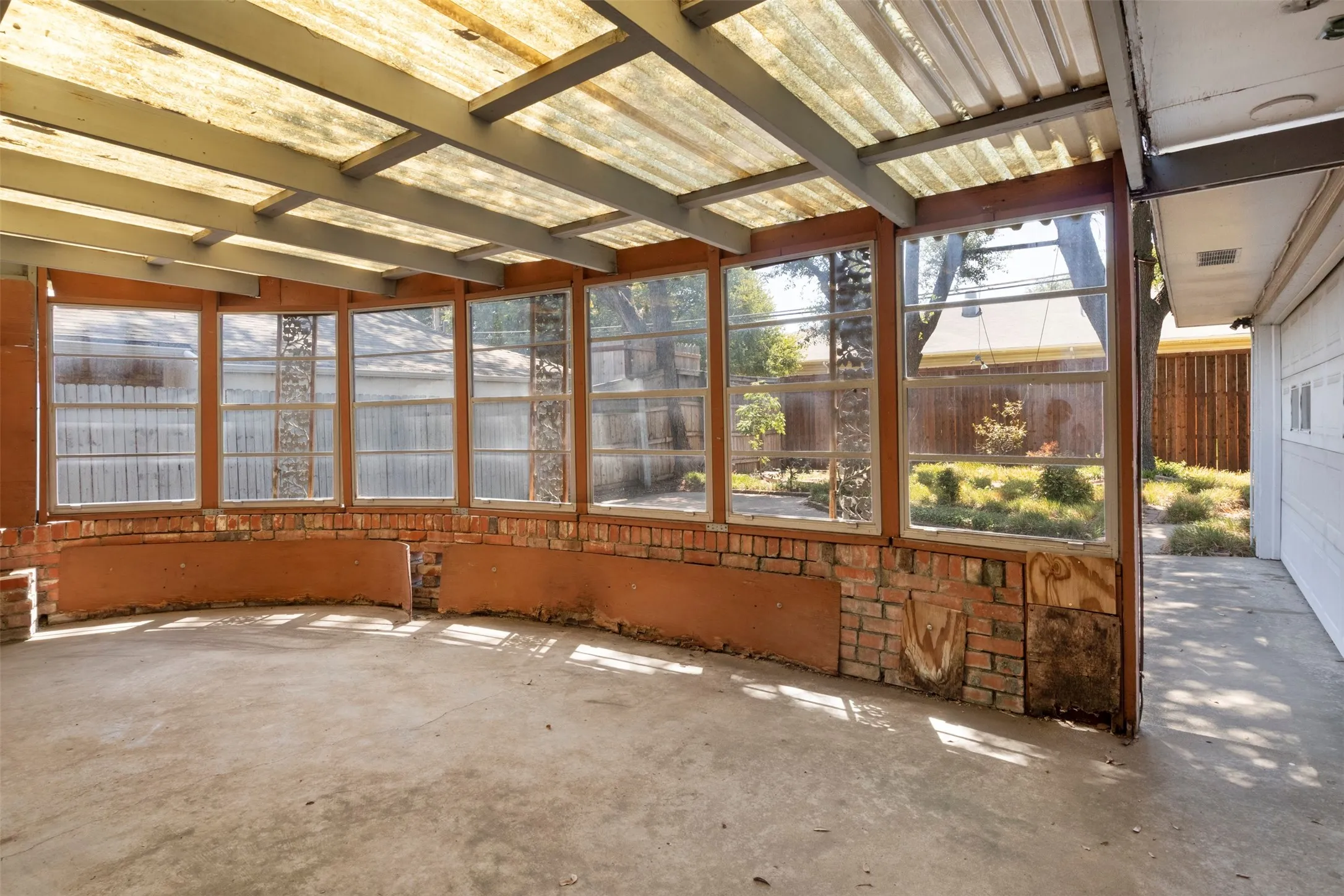 Enclosed patio with a transparent roof, concrete flooring, and brick wall accents