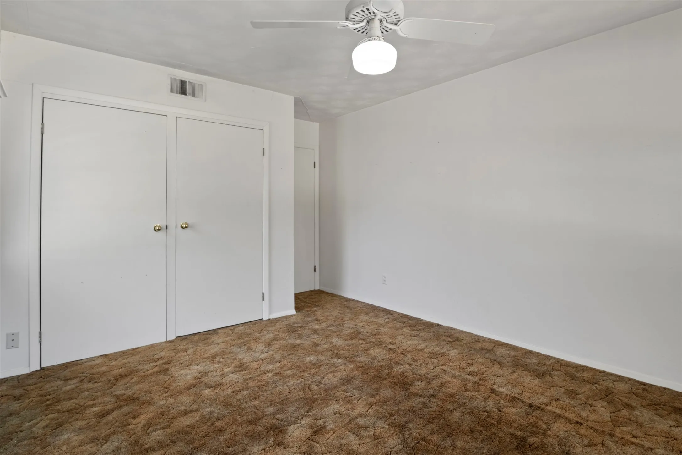 White walls with white trim, brown carpet, ceiling fan with integrated lighting, and white bi-fold closet doors