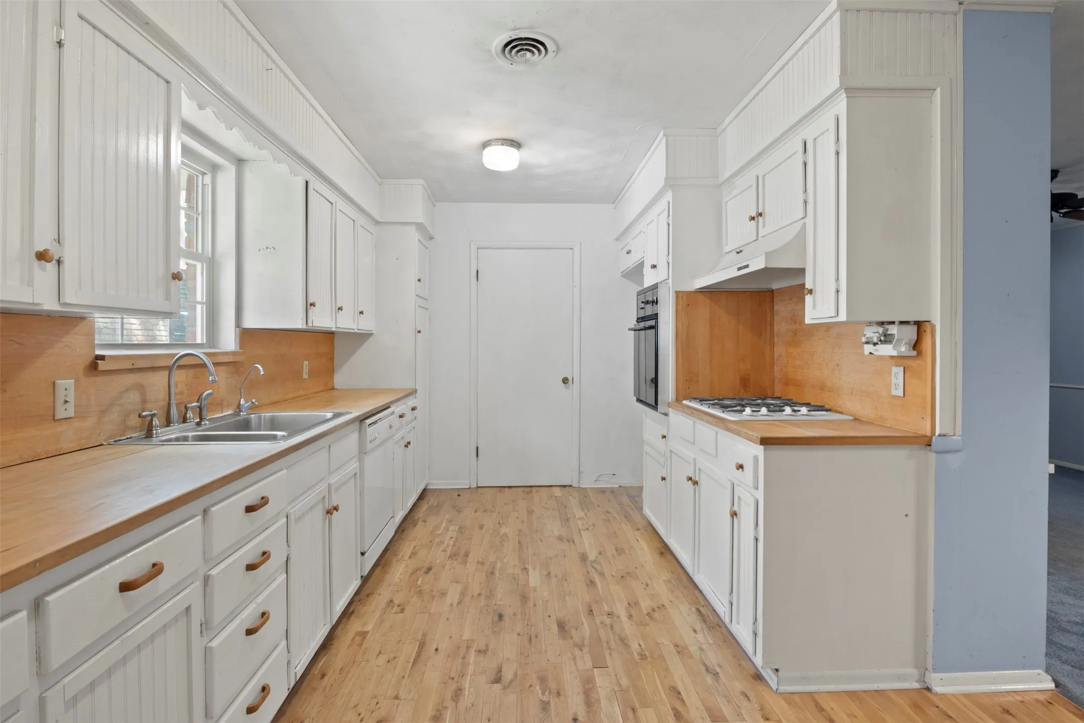U-shaped kitchen with wood-finish flooring, white cabinetry, integrated dual basin sink, and built-in oven with gas cooktop