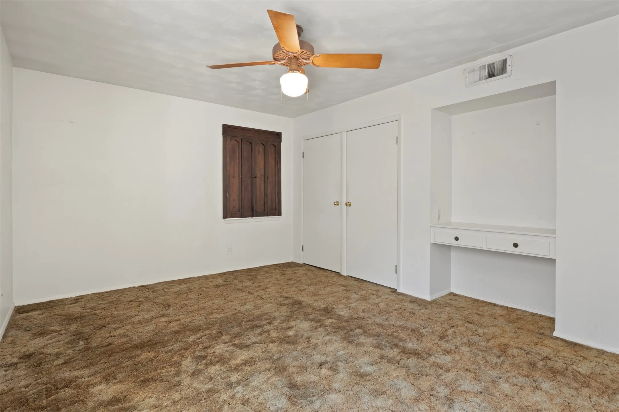Ceiling fan with light fixture, built-in cabinetry with two drawers, integrated closet with bi-fold doors, and a wood-paneled window