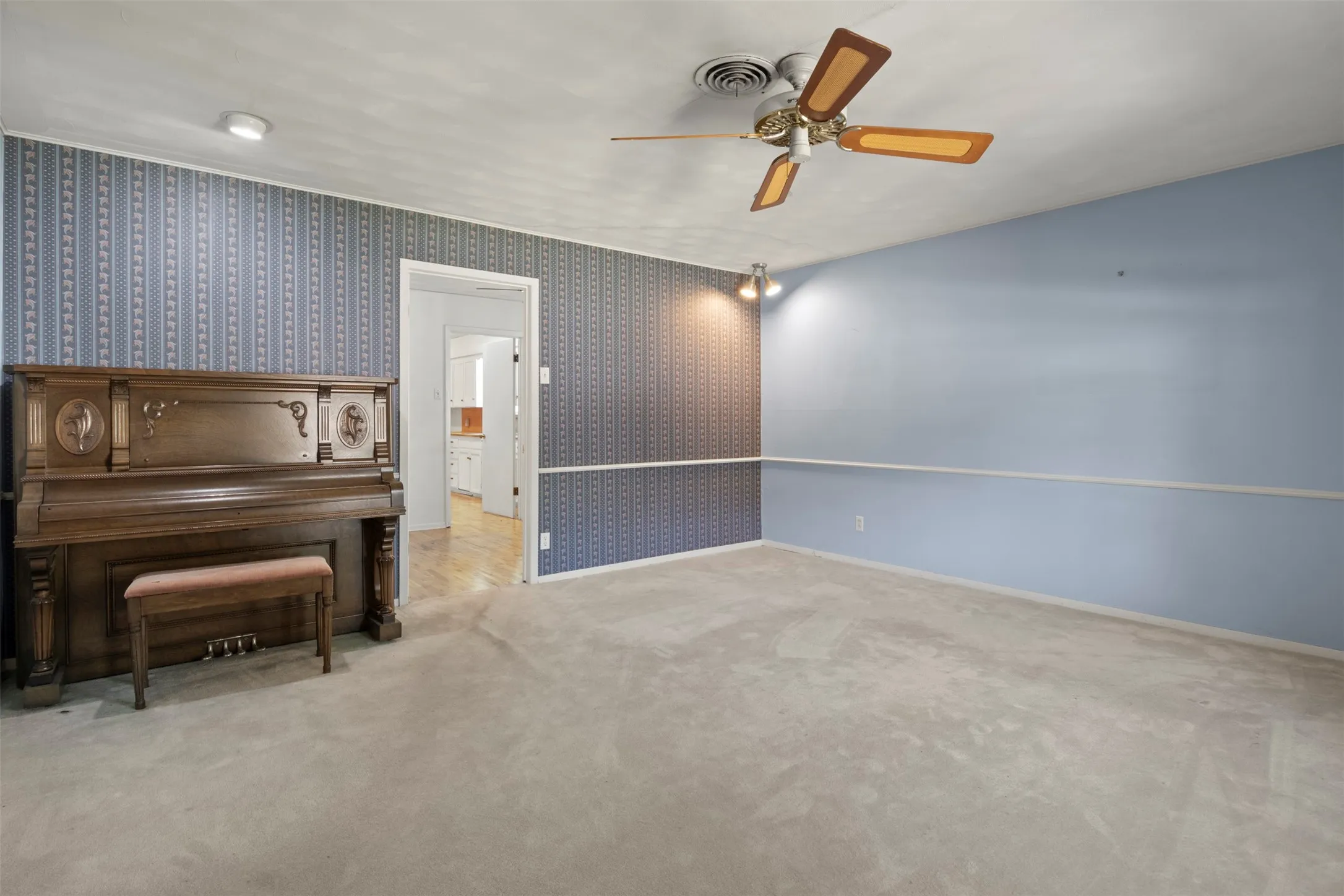 Recessed lighting, ceiling fan, textured wallpaper accent wall, wood-finish flooring visible through doorway, soft carpet