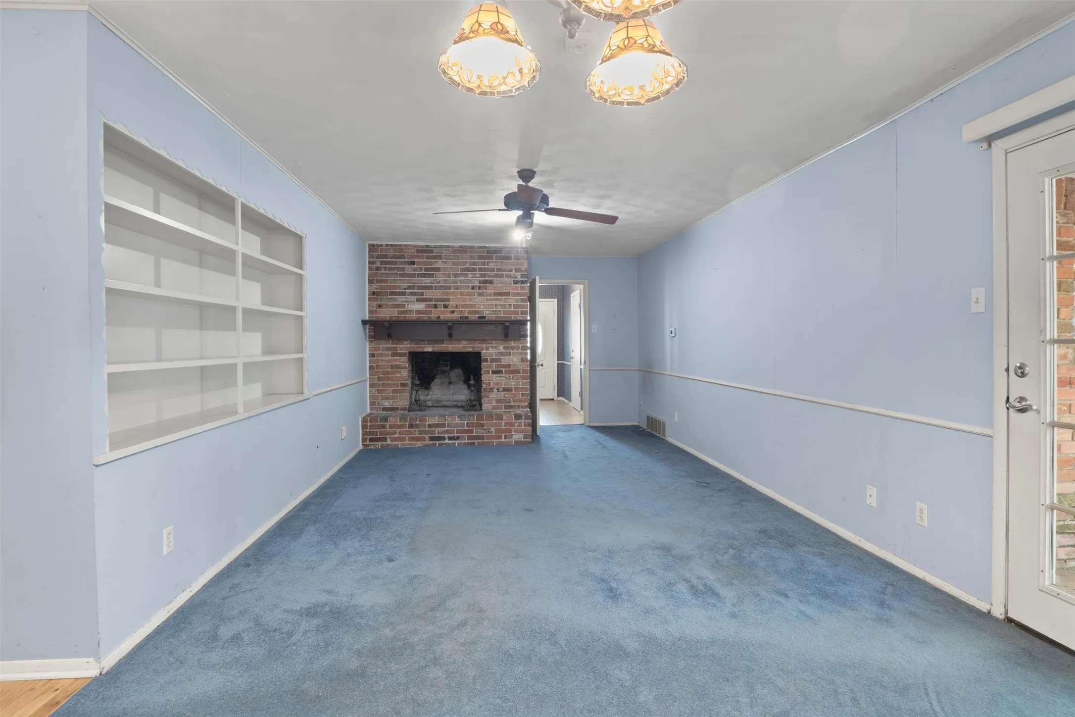 Built-in shelving, brick fireplace with mantel, ceiling fan, and decorative overhead lighting