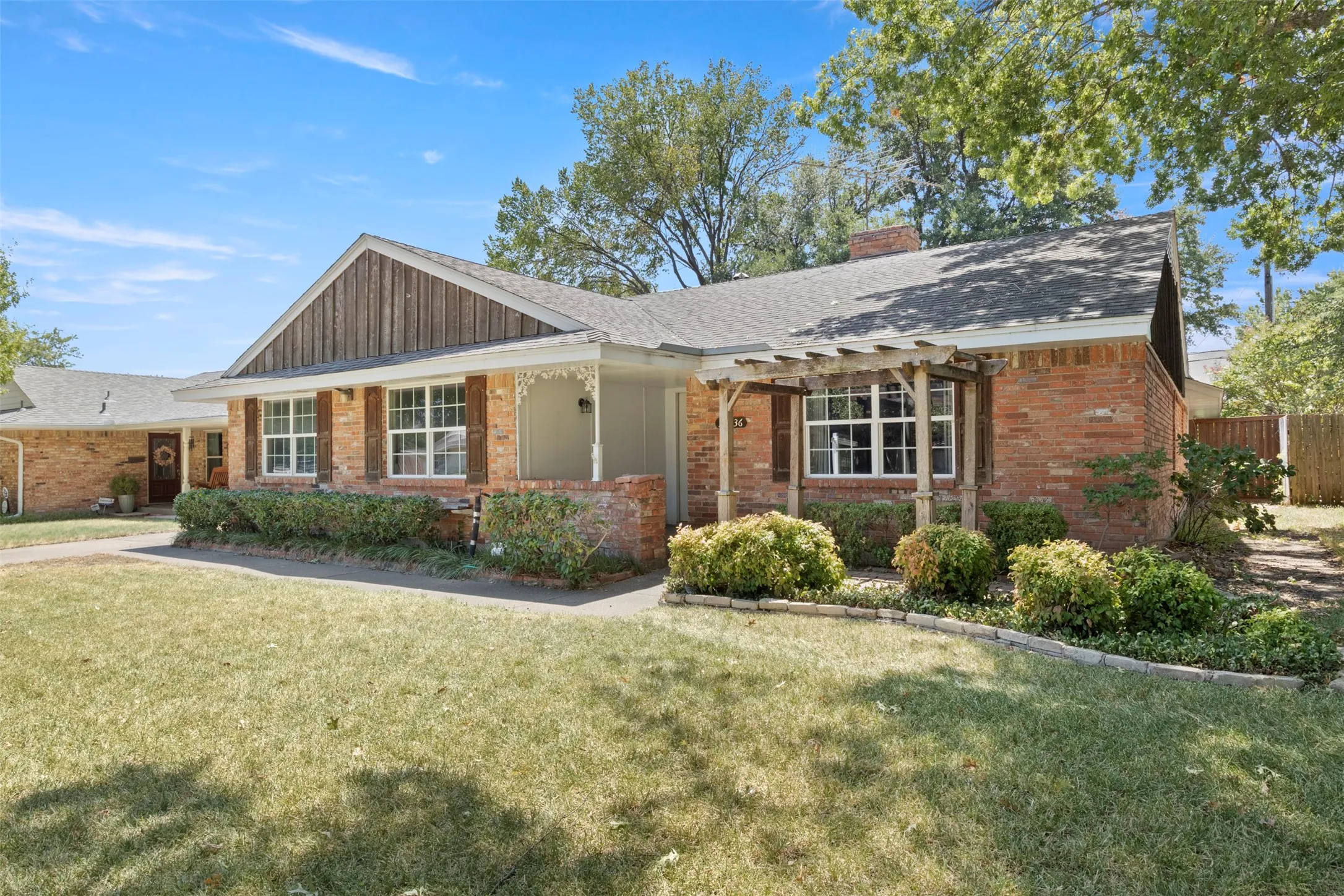 Brick exterior with wood shutters, front porch with decorative railing, and an integrated pergola