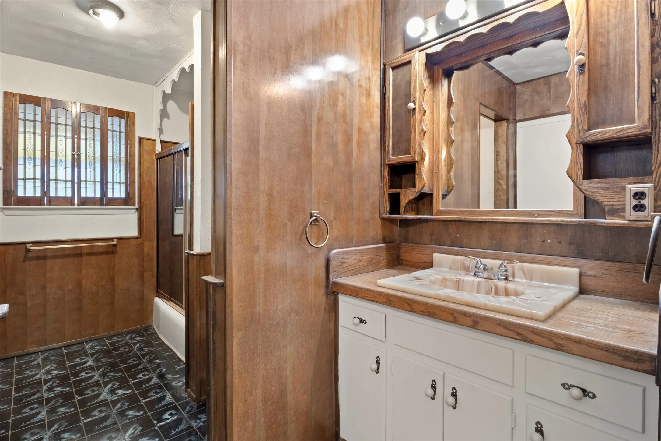 Built-in vanity with a stone-finish countertop and basin, wood-paneled walls, and patterned floor tiling