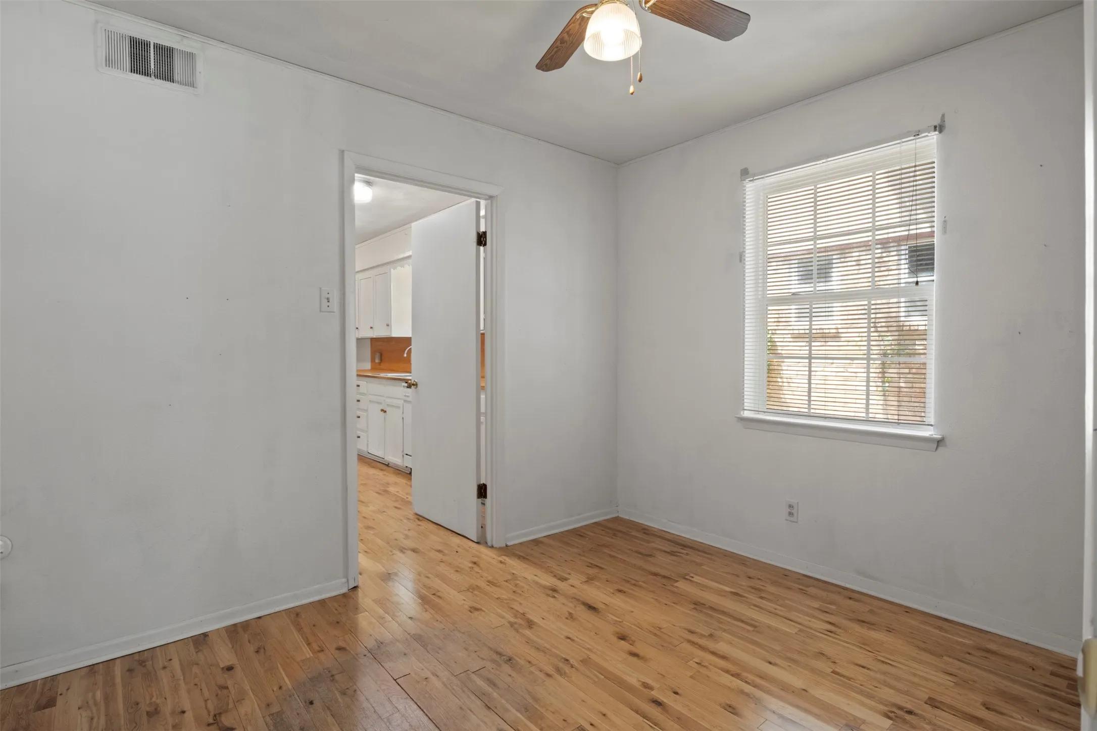 Wood-finish flooring throughout, white walls, and a window with blinds