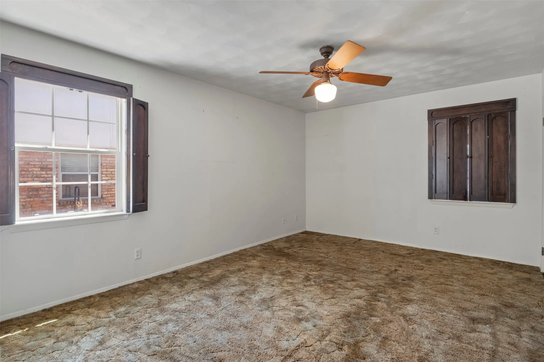 Ceiling fan with integrated lighting, wood-finish window shutters, and a window with exterior brick exposure