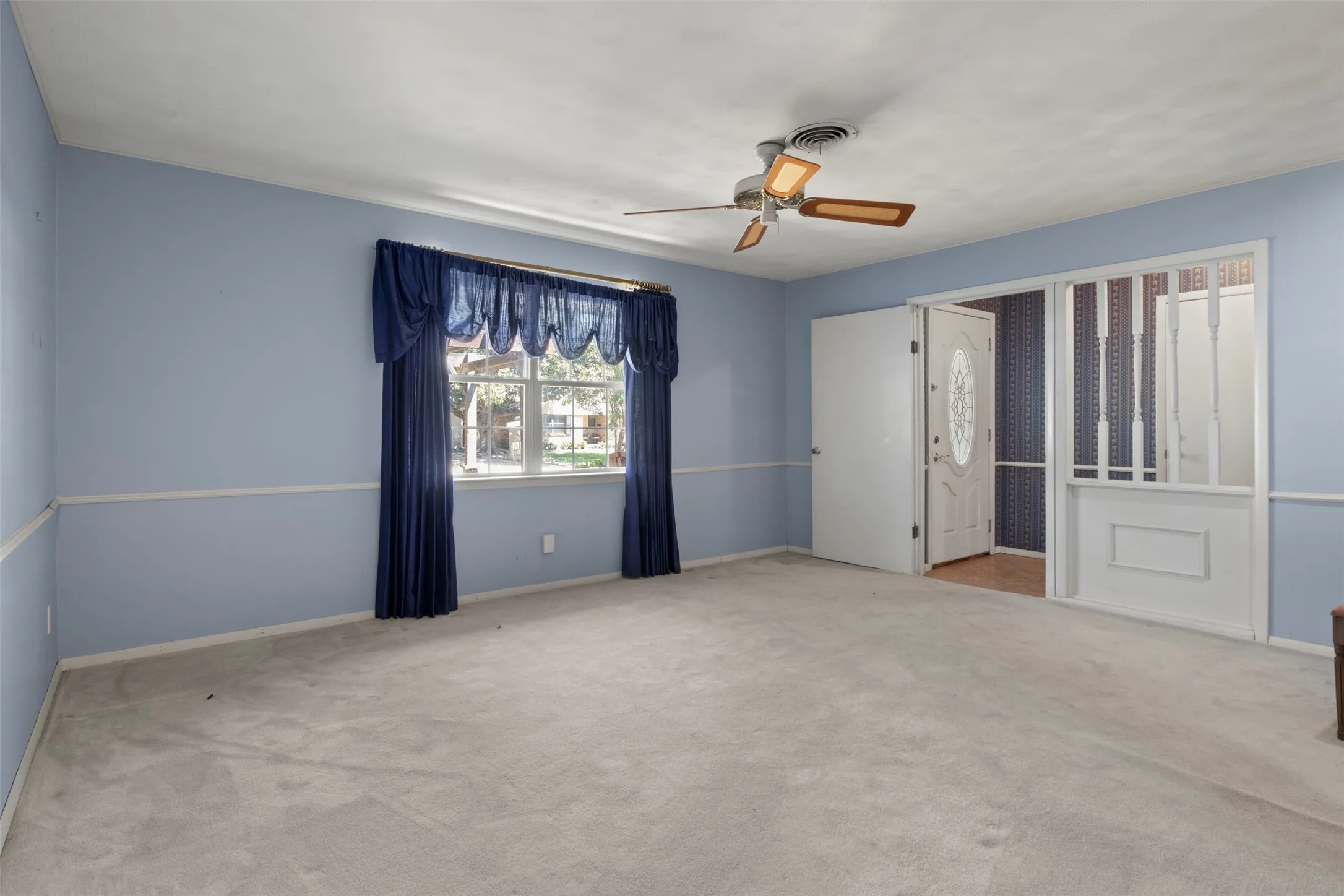Carpeted room featuring a ceiling fan, a window with exterior views, and a paneled entry door with decorative glass