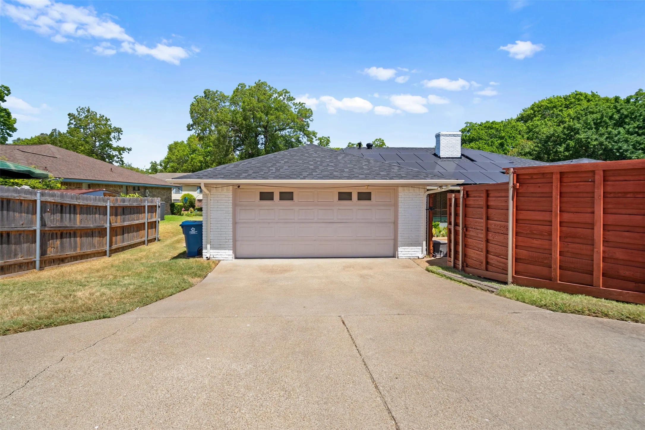 Attached two-car garage with a concrete driveway, white brick exterior, and a dark shingle roof