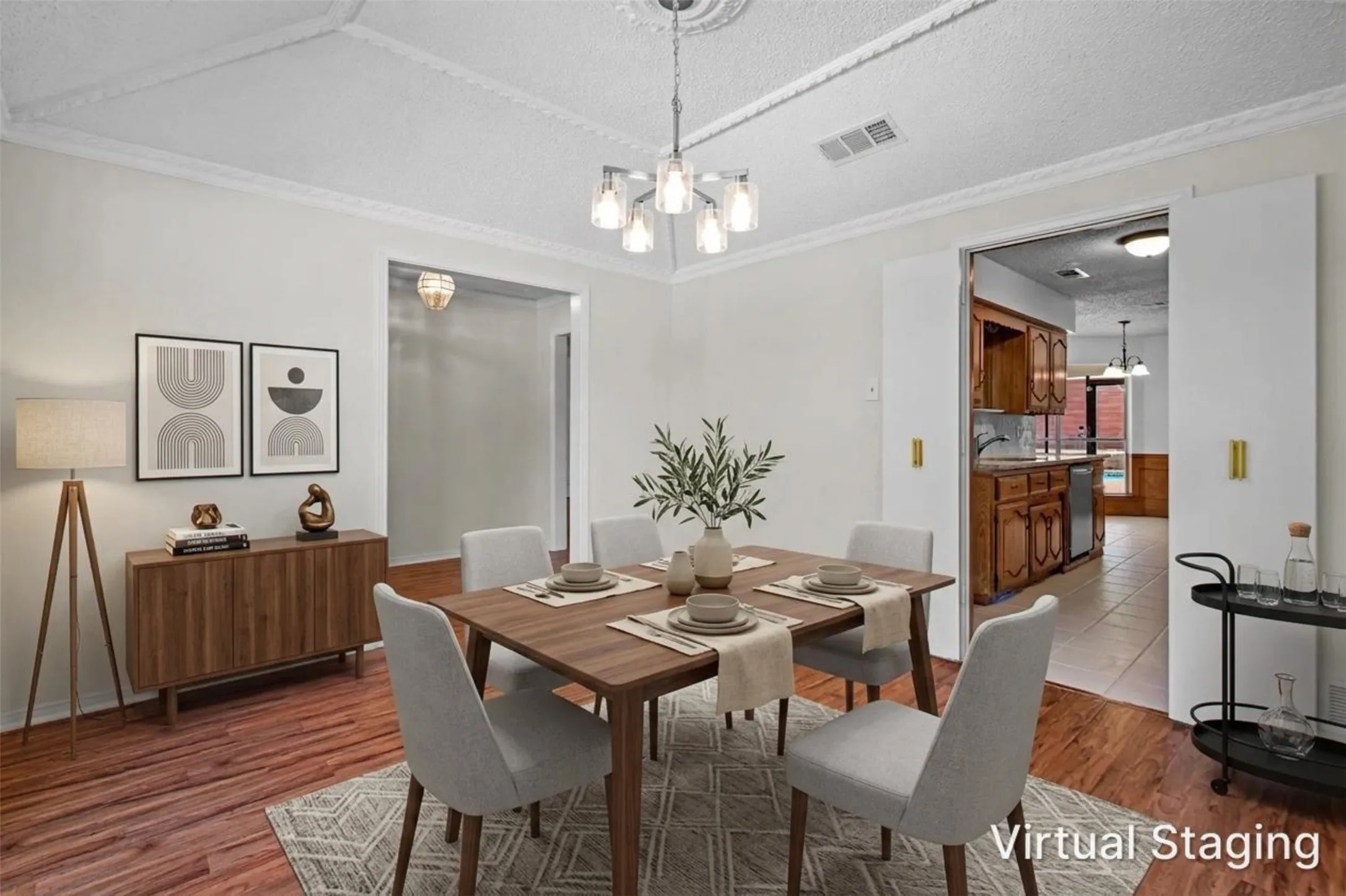 Wood-finish flooring, recessed ceiling with decorative molding, modern chandelier, double pocket doors, and a built-in kitchen
