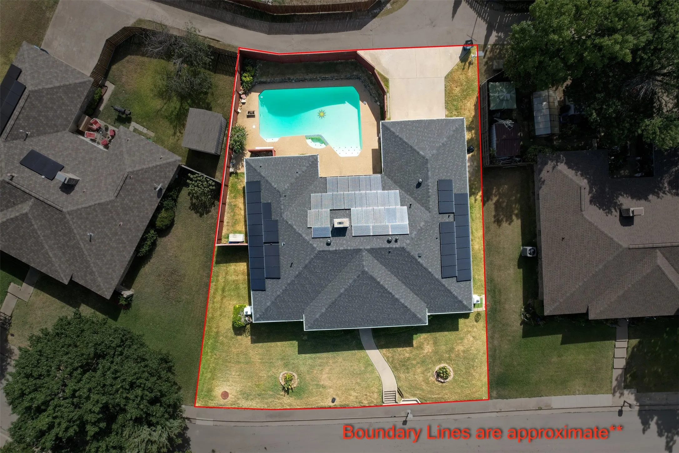 Shingled roof with solar panels, backyard swimming pool, concrete pool deck, attached driveway, and a manicured lawn