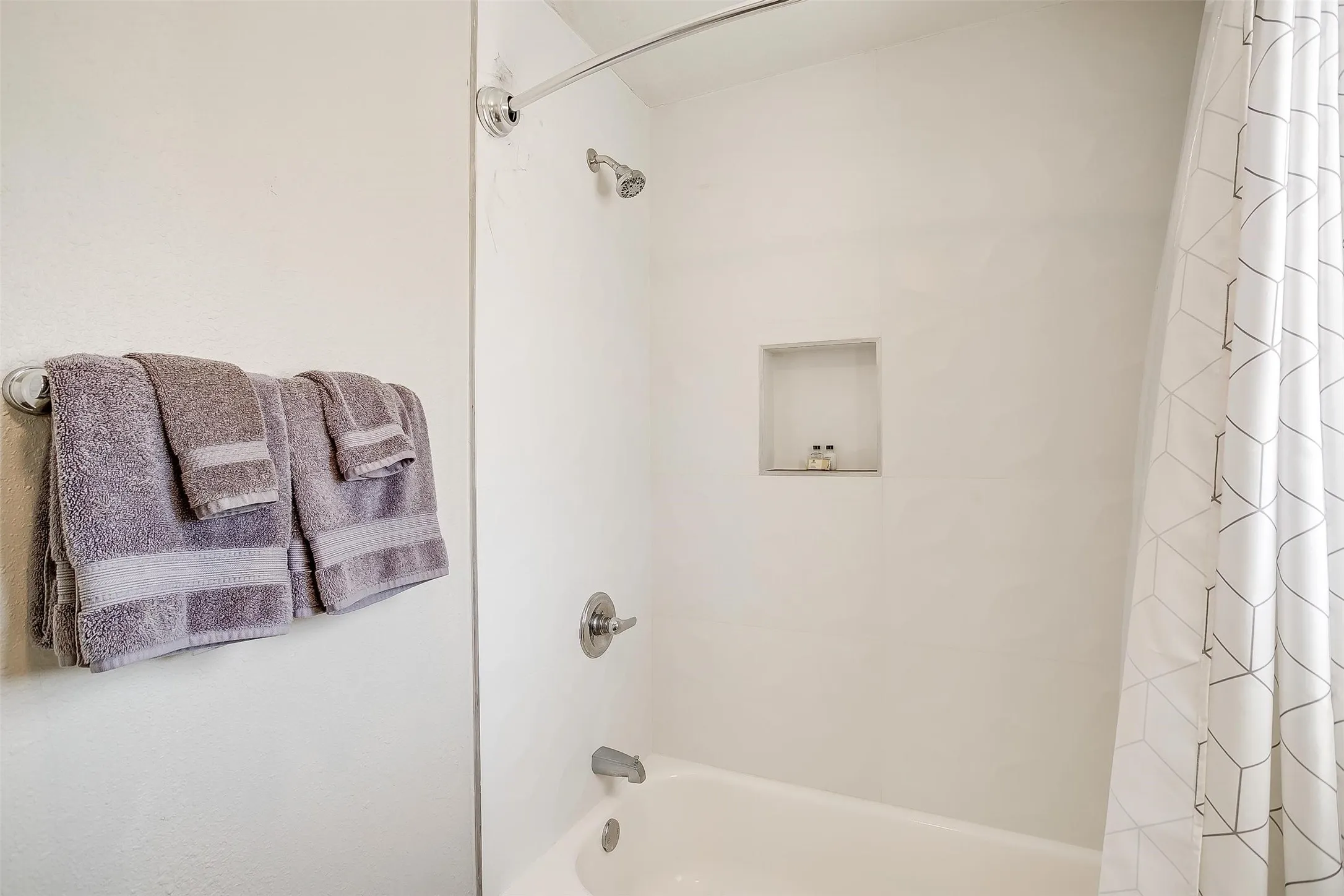 Bathtub/shower combination featuring a built-in shower niche, chrome fixtures, and a curved shower rod